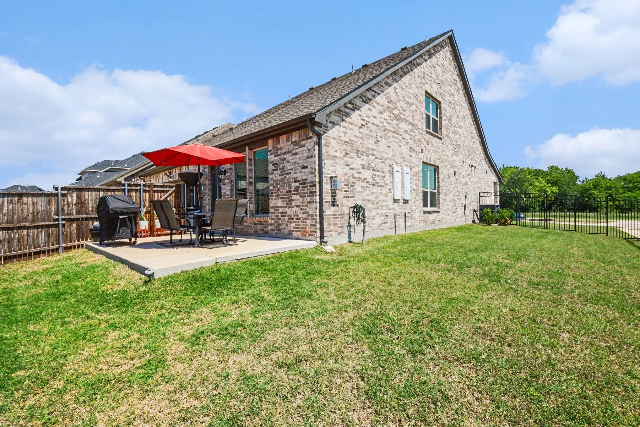 Spacious backyard featuring a concrete patio, a privacy fence, and a black wrought iron fence bordering a tree-lined perimeter