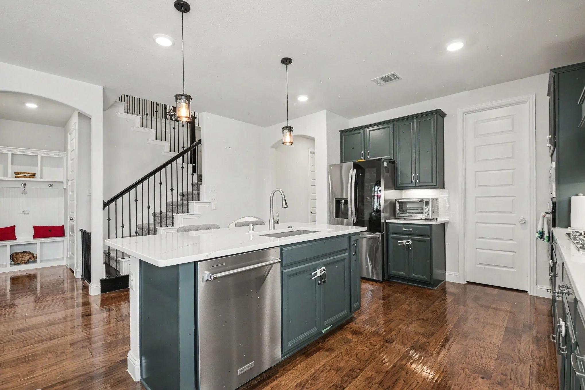 Gourmet kitchen featuring a central island with integrated stainless steel dishwasher, white countertops, dark cabinetry, and wood-finish flooring