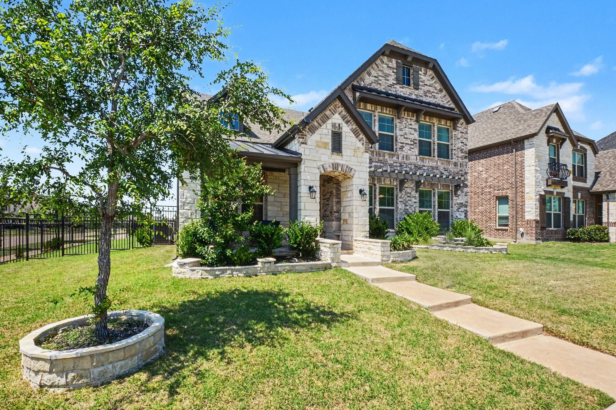 Stone and brick facade residence with a covered entry, multiple gables, and a wrought iron fence