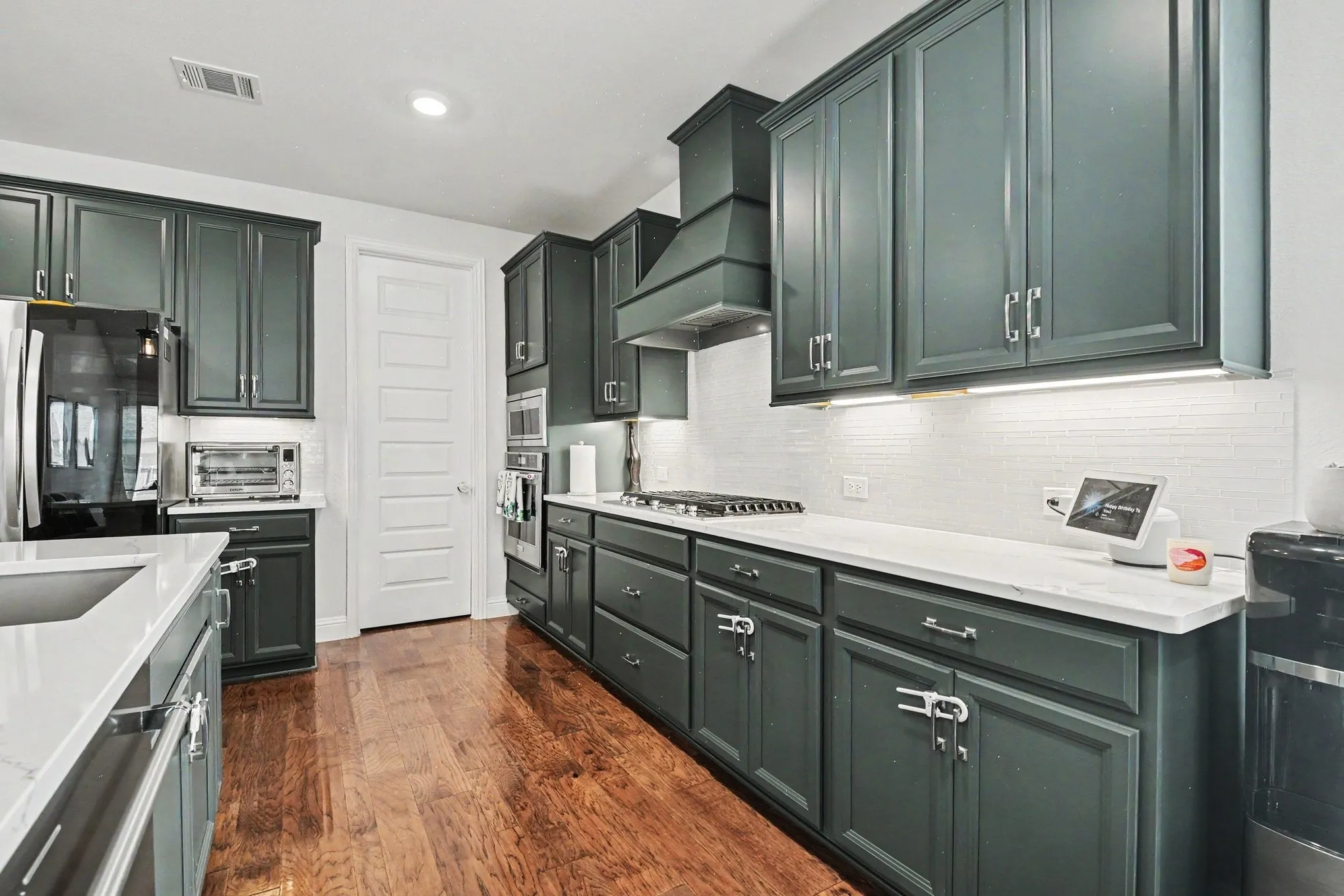 Kitchen featuring dark cabinetry, white countertops, wood-finish flooring, stainless steel appliances, and a tile backsplash