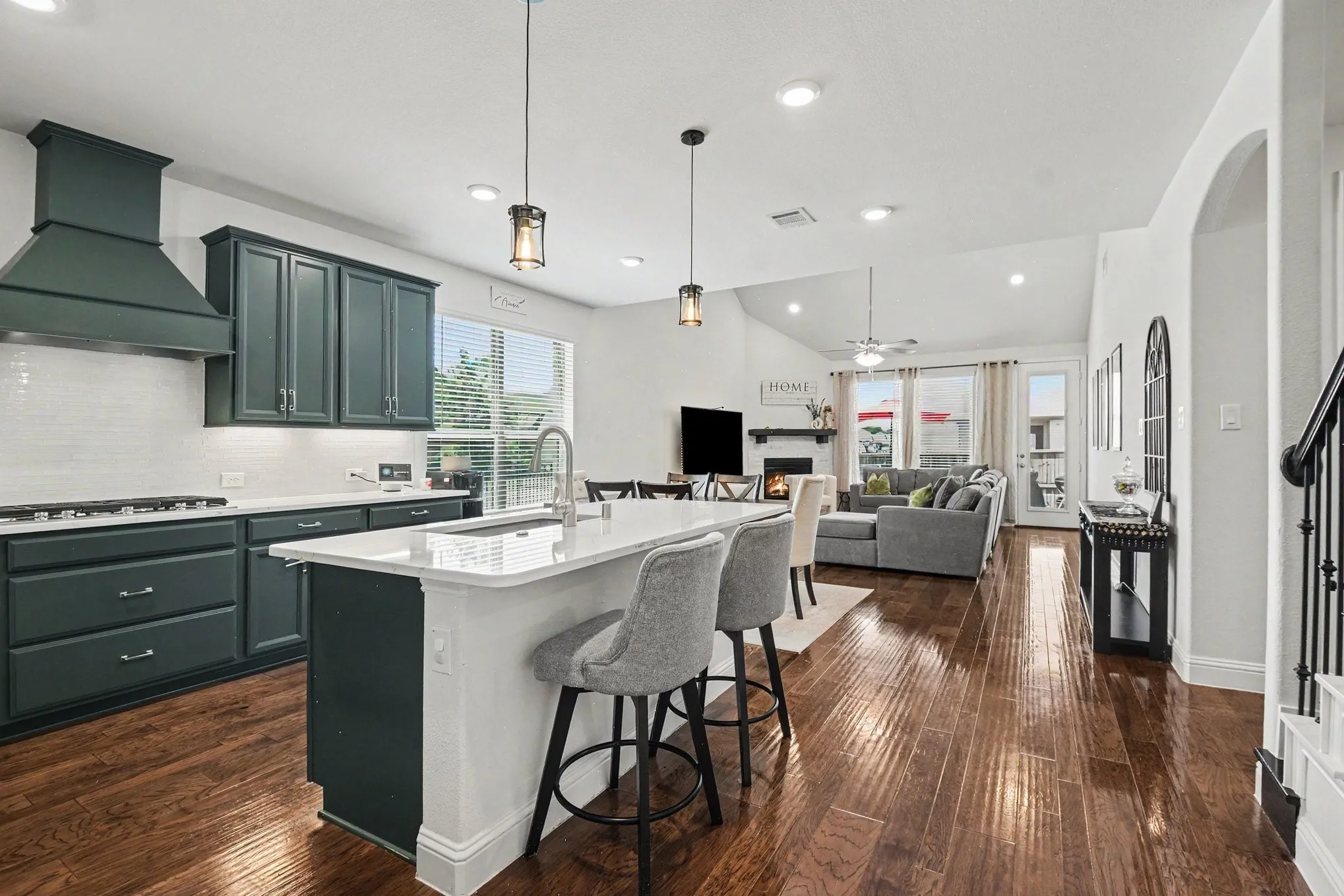 Open-concept living space featuring a kitchen island with seating, dark wood-finish flooring, a vaulted ceiling, recessed lighting, and a fireplace with a mantel