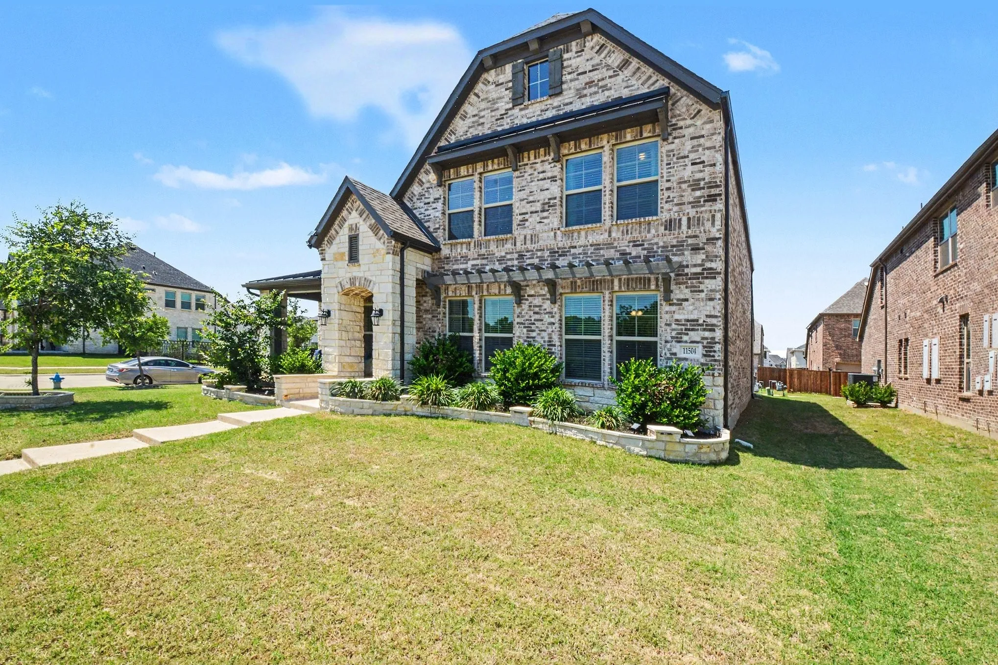 Two-story residence featuring a combination of brick and stone facade, a covered entry, and multiple windows