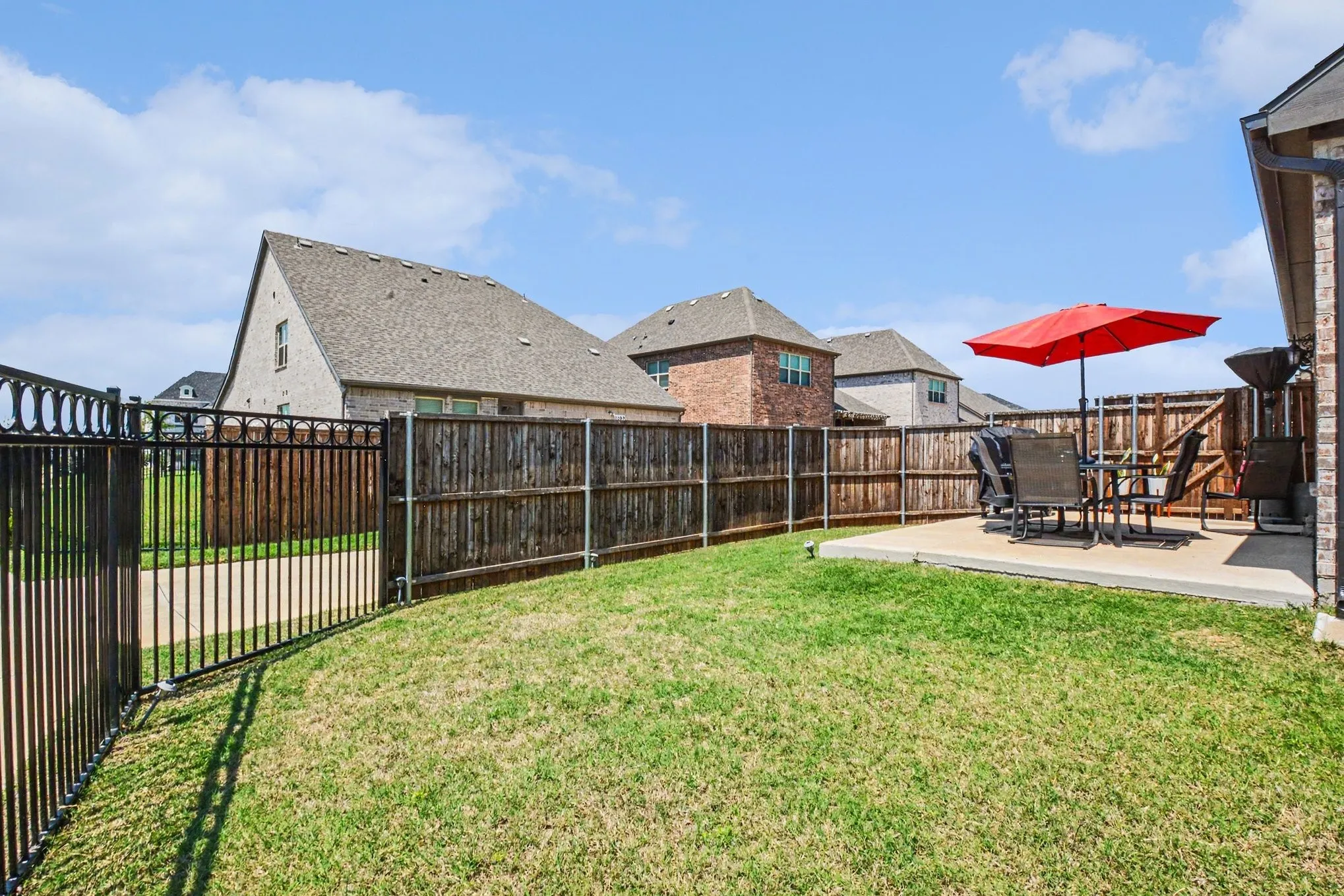 Fenced backyard featuring a concrete patio, a wrought-iron gate, and wood privacy fencing