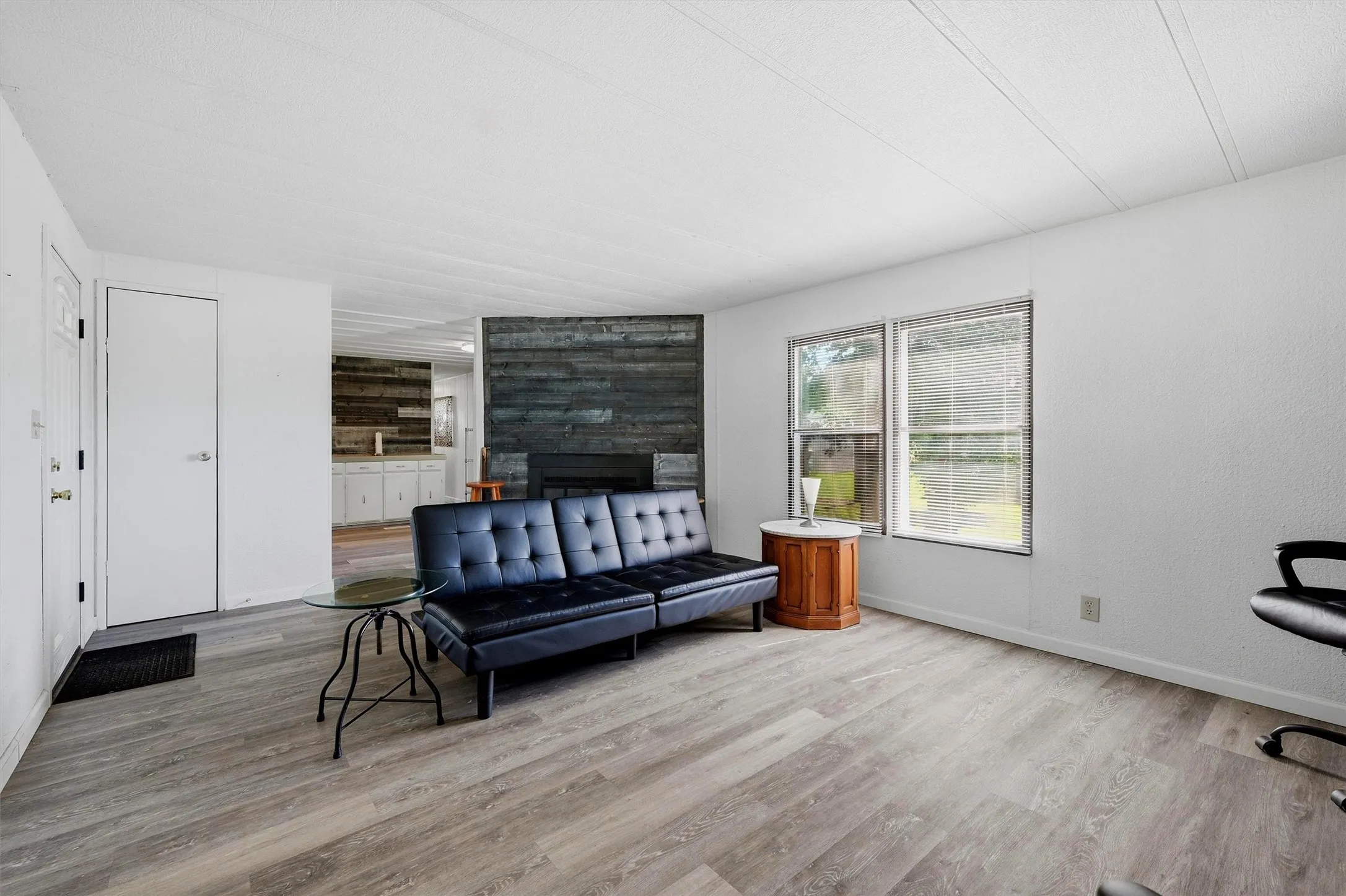 Living area featuring wood-finish flooring, white painted walls, and a fireplace with a horizontal shiplap surround