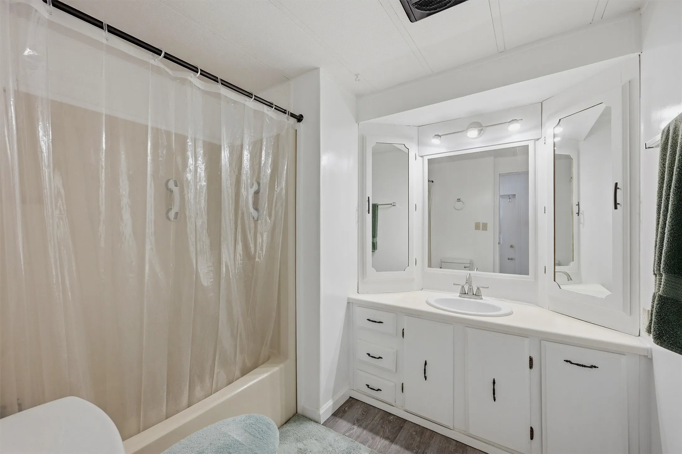Bathroom vanity with white cabinetry, a single basin sink, and a multi-panel mirrored medicine cabinet