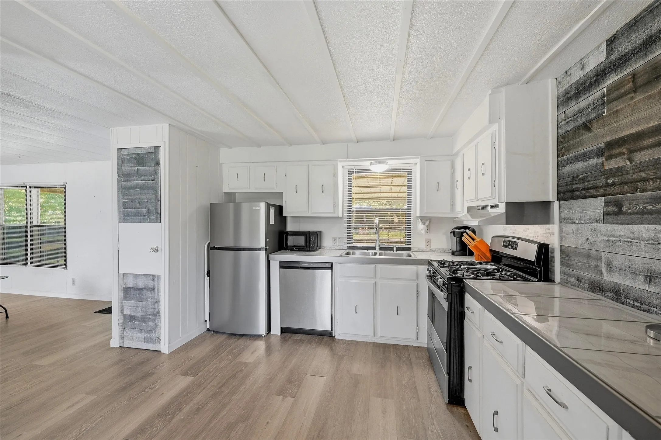 Kitchen featuring white cabinetry, tile countertops, stainless steel refrigerator, stainless steel dishwasher, and gas range
