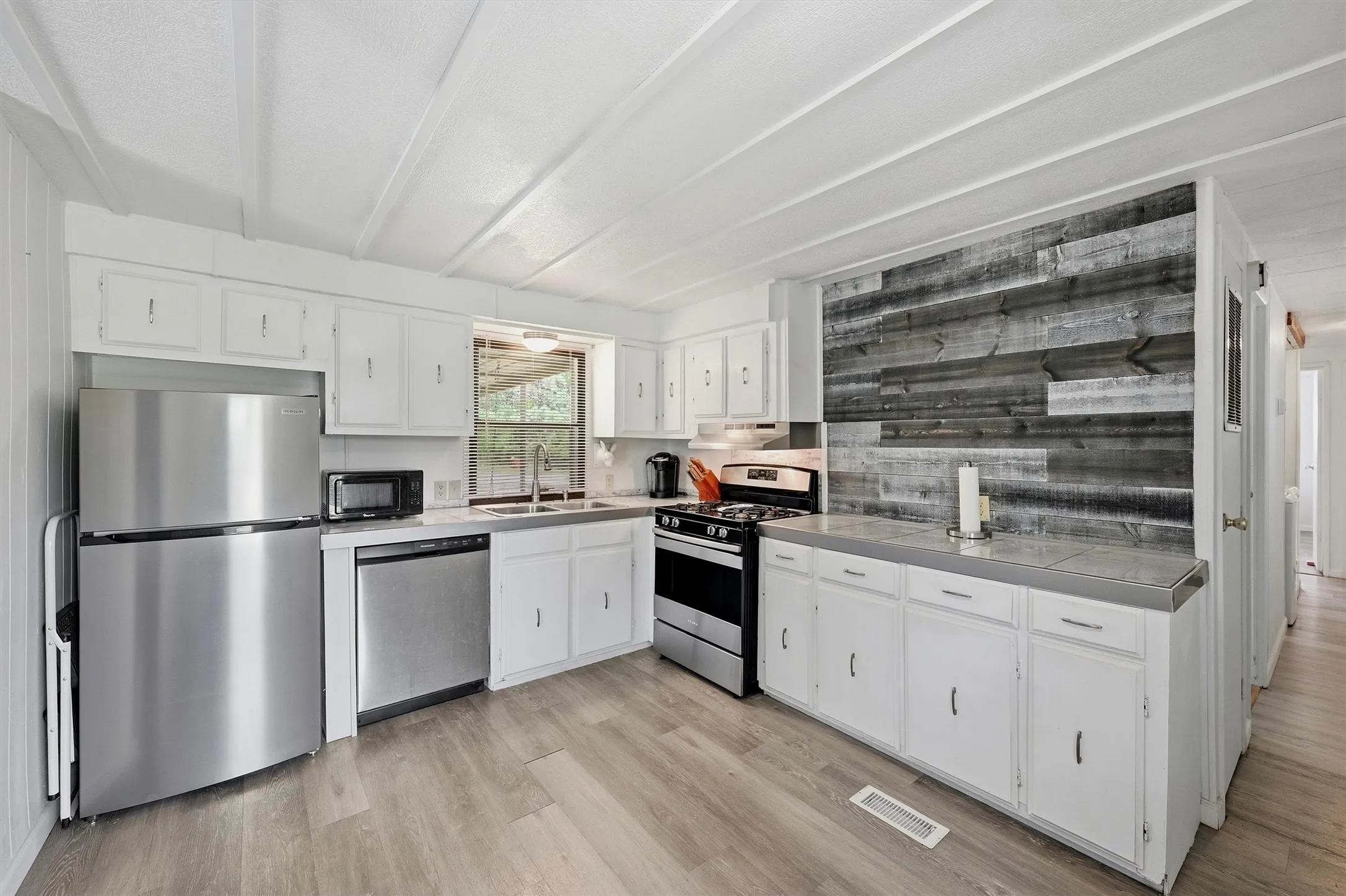 Kitchen featuring wood-finish flooring, white cabinetry, stainless steel appliances, and a wood plank accent wall