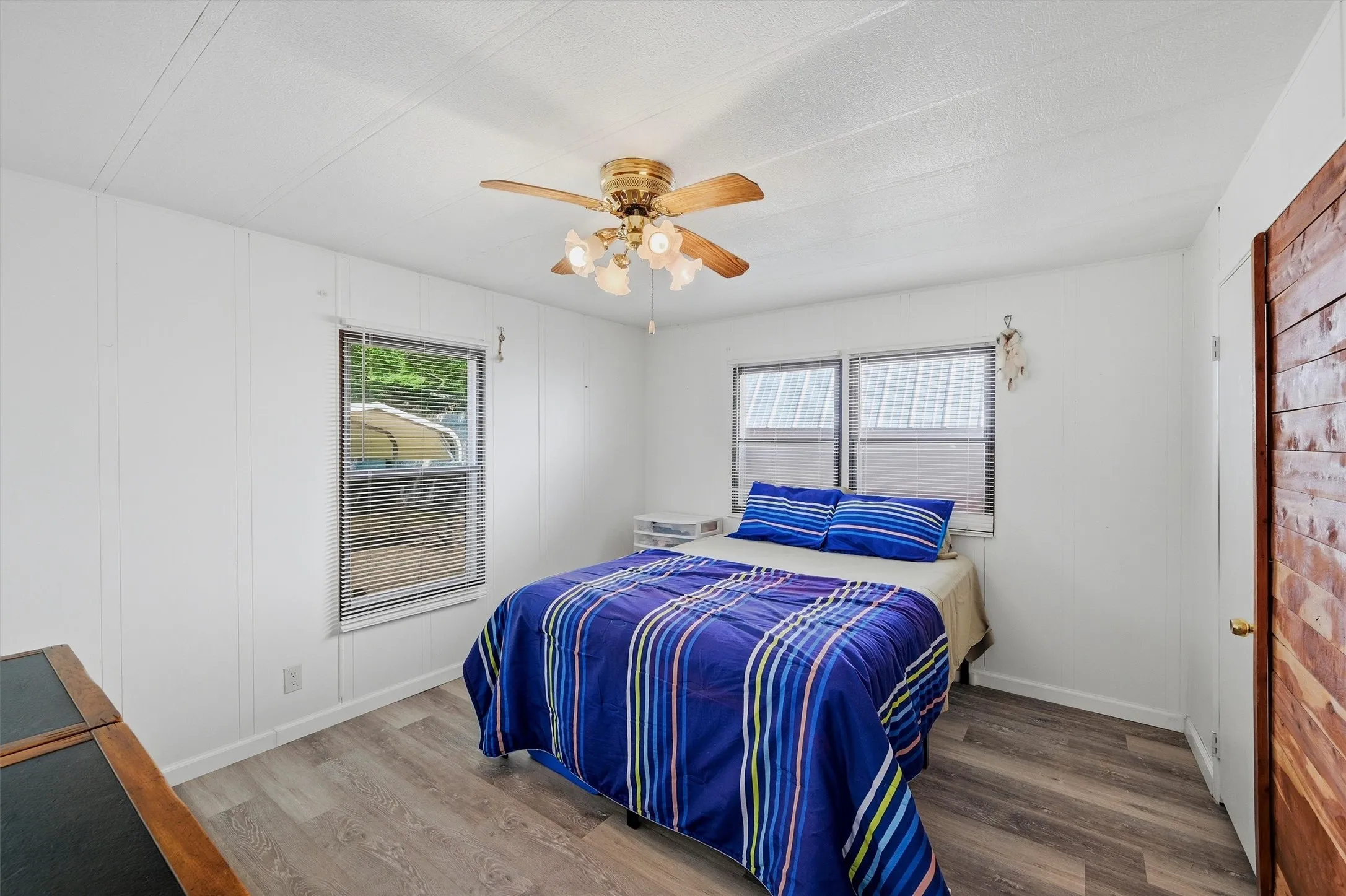 Spacious room featuring wood-finish flooring, white paneled walls, and a ceiling fan with integrated lighting