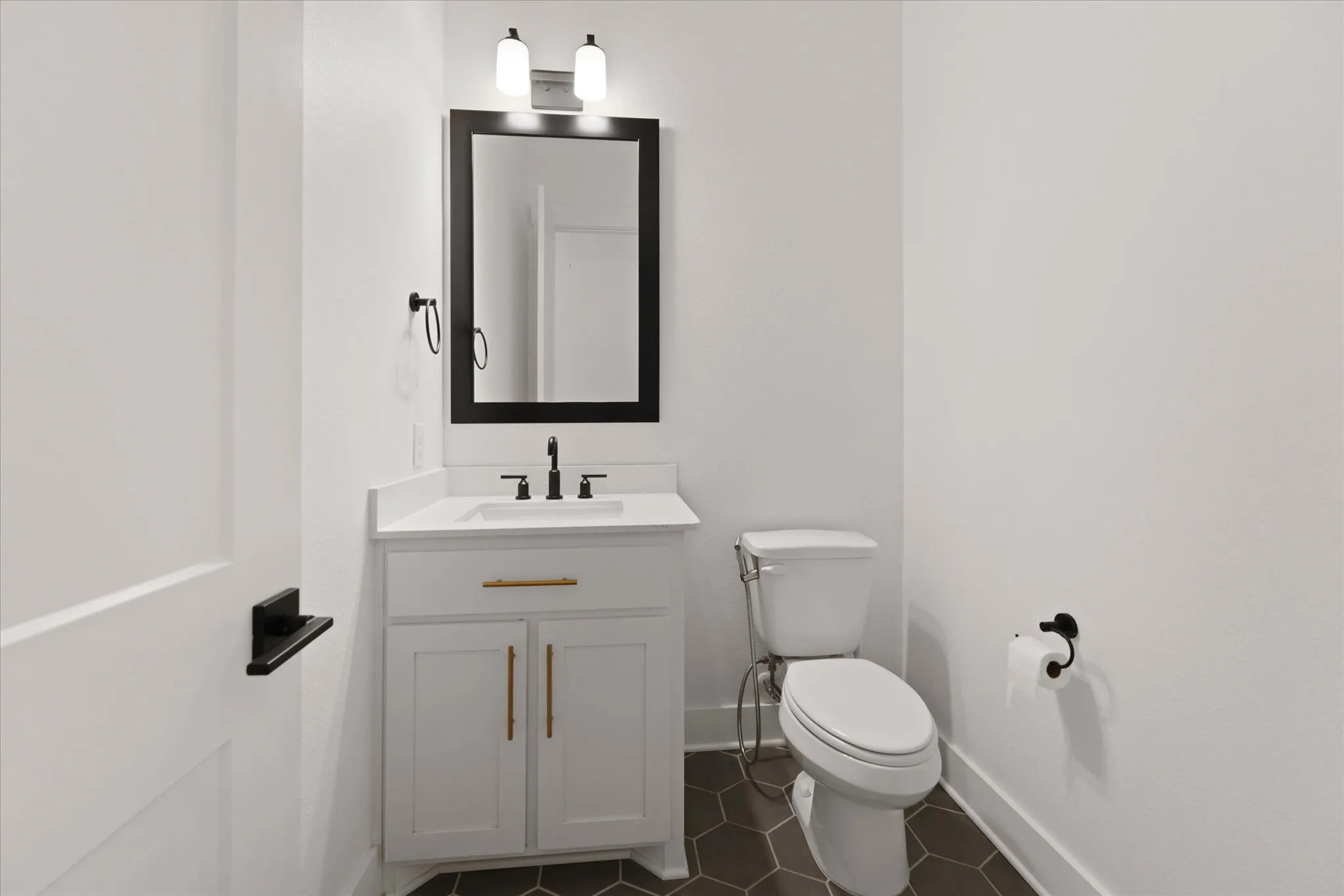 Powder room featuring a white vanity with gold-tone hardware, a rectangular undermount sink, a dark framed mirror, and matte black fixtures