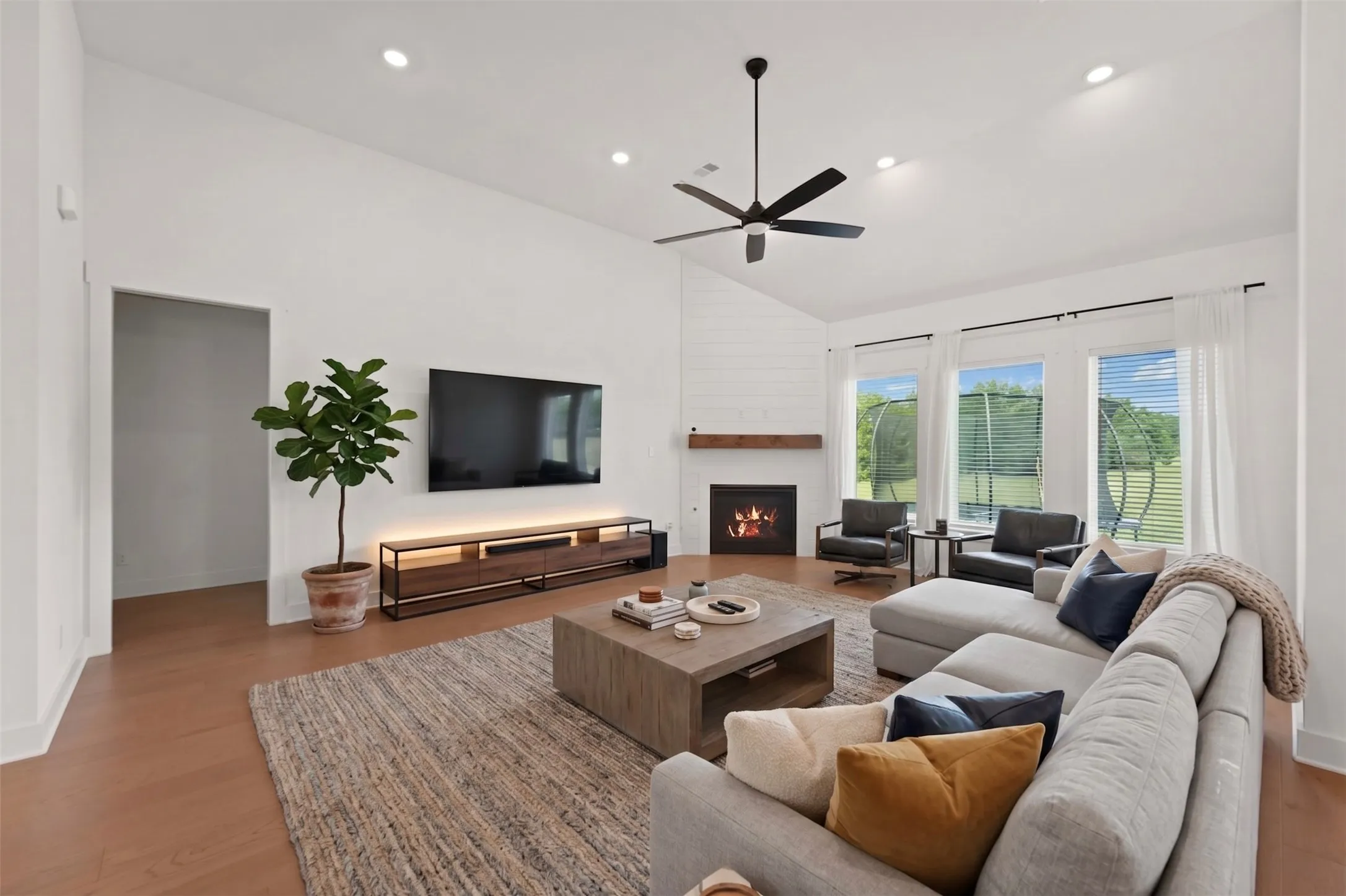Spacious living area featuring a vaulted ceiling with recessed lighting, wood-finish flooring, a contemporary ceiling fan, and a fireplace with a wood mantel