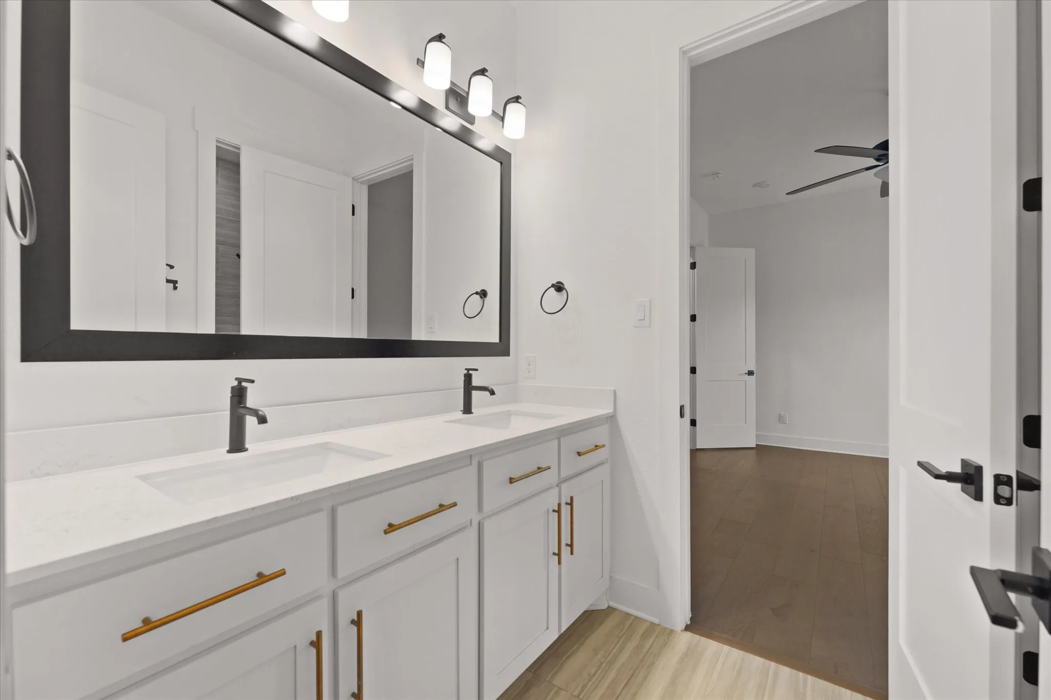 Bathroom featuring a double vanity with white cabinetry, gold-finish hardware, and a white countertop