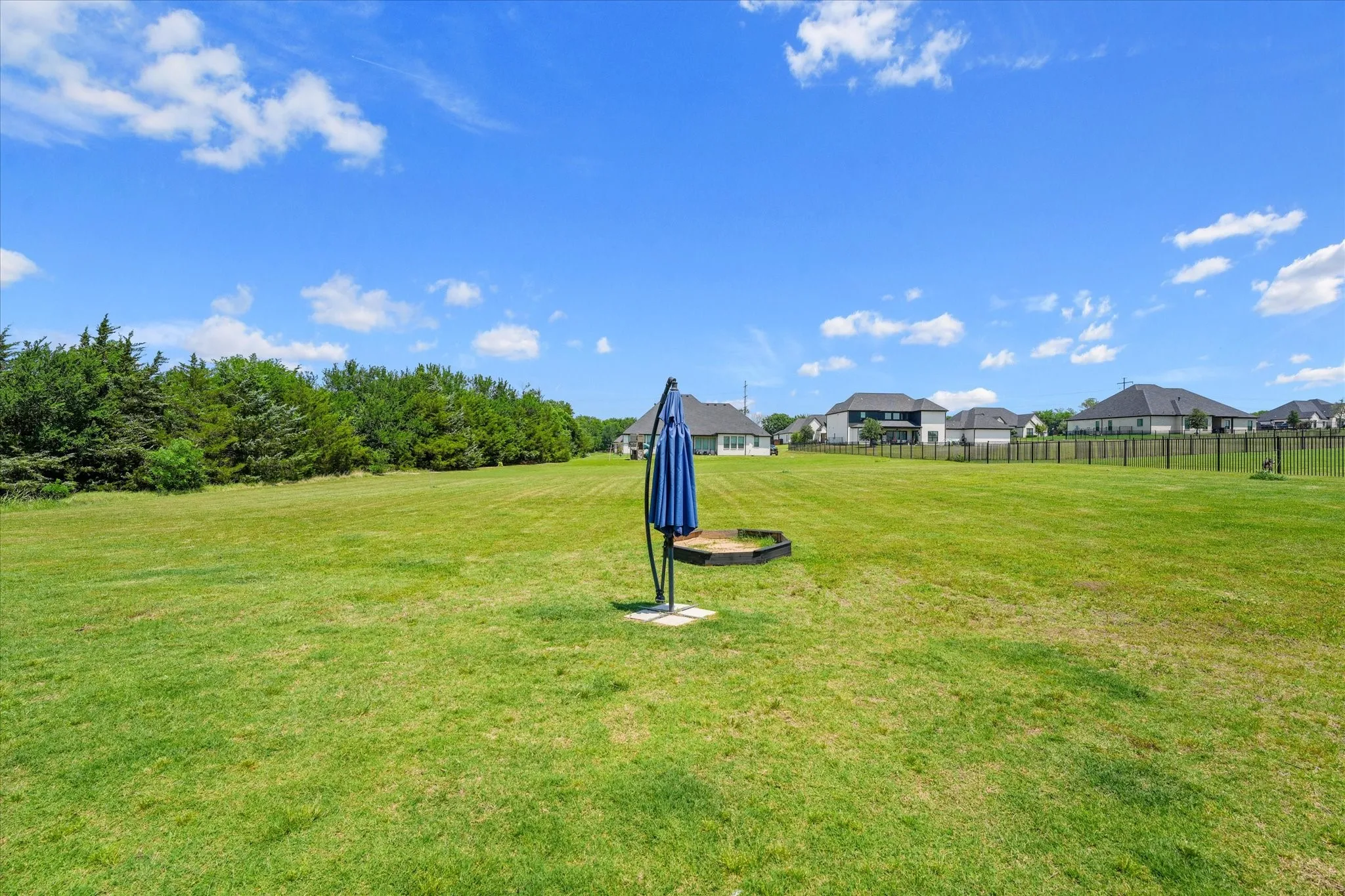 Expansive grassy area featuring a tree line at one boundary and partial fencing