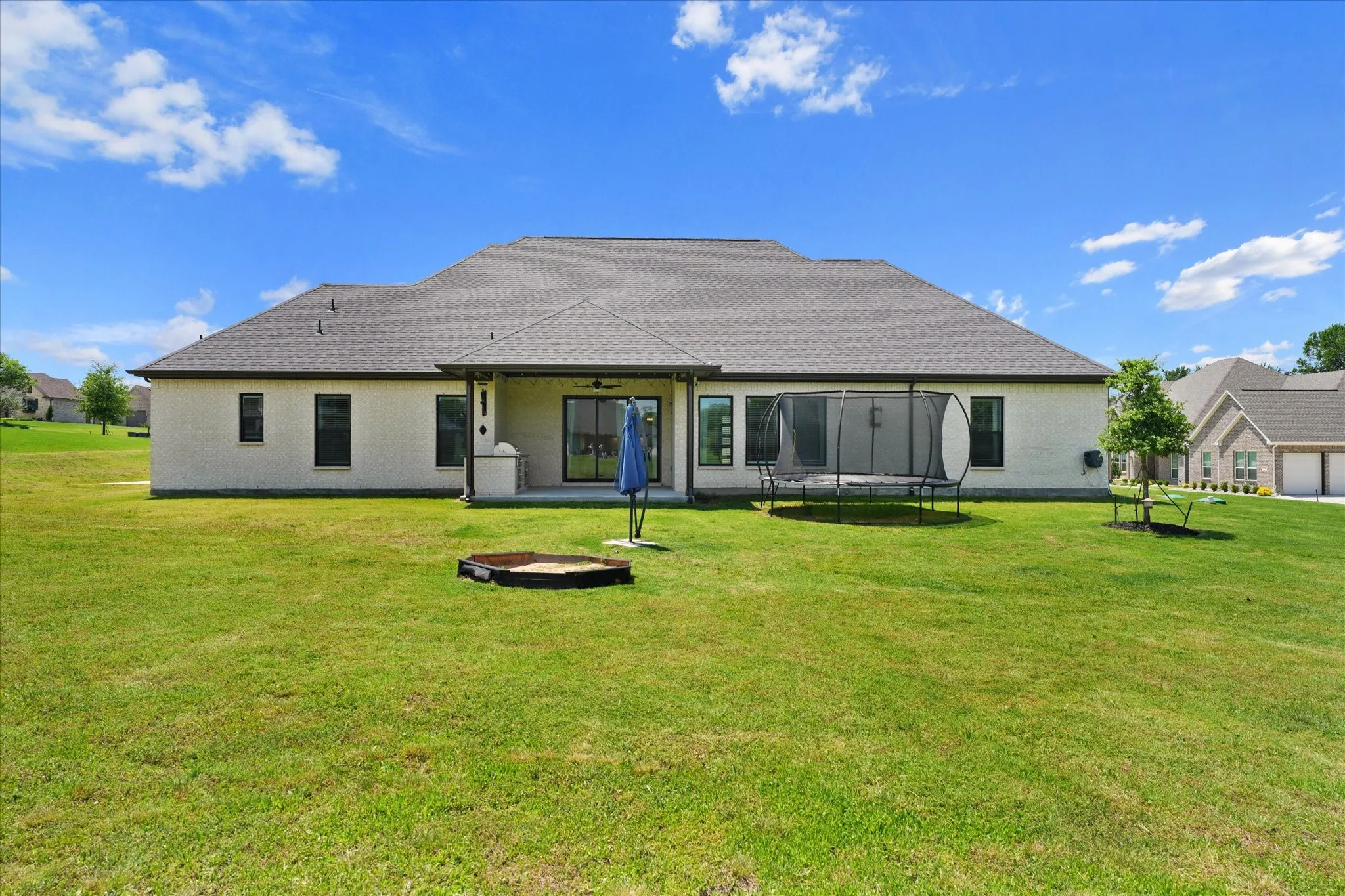 Expansive green lawn surrounds the rear exterior of this property, featuring a covered patio with a sliding glass door and an additional window
