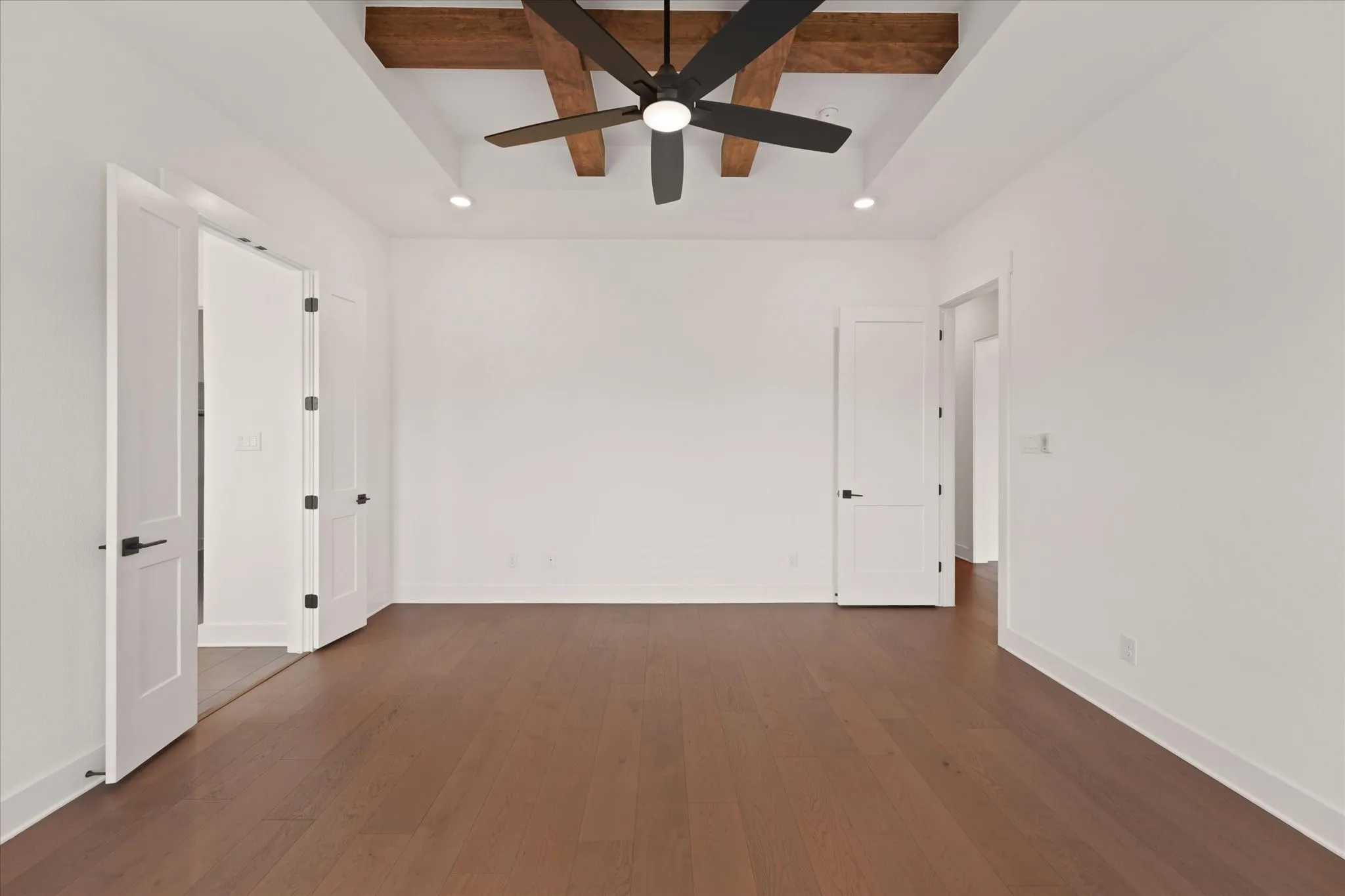 Spacious Primary Bedroom featuring wood-finish flooring, white walls, and a tray ceiling with exposed wood beams