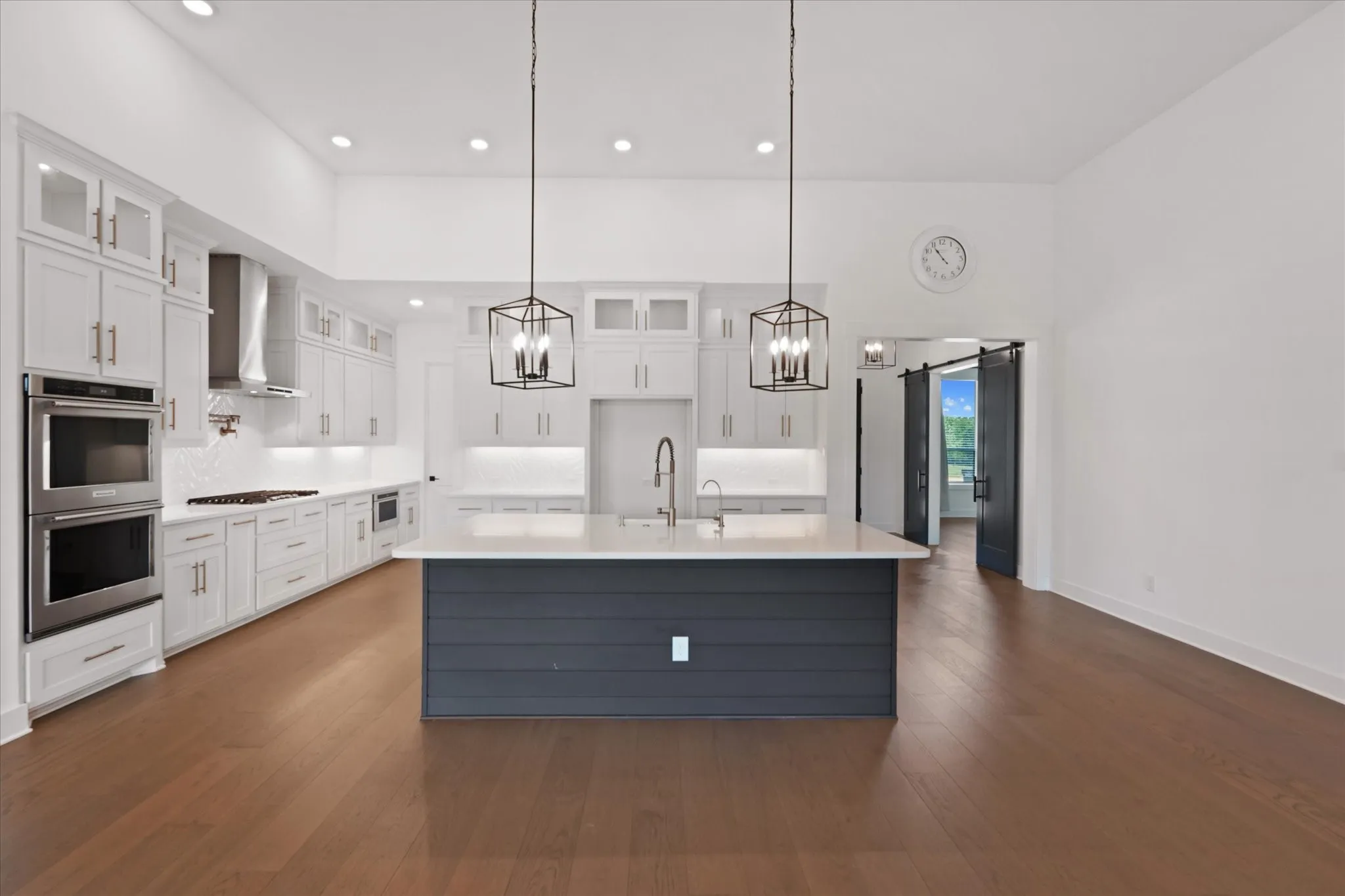 Expansive kitchen featuring white cabinetry, stainless steel double wall ovens, a large center island with a white countertop, and two black geometric pendant lights