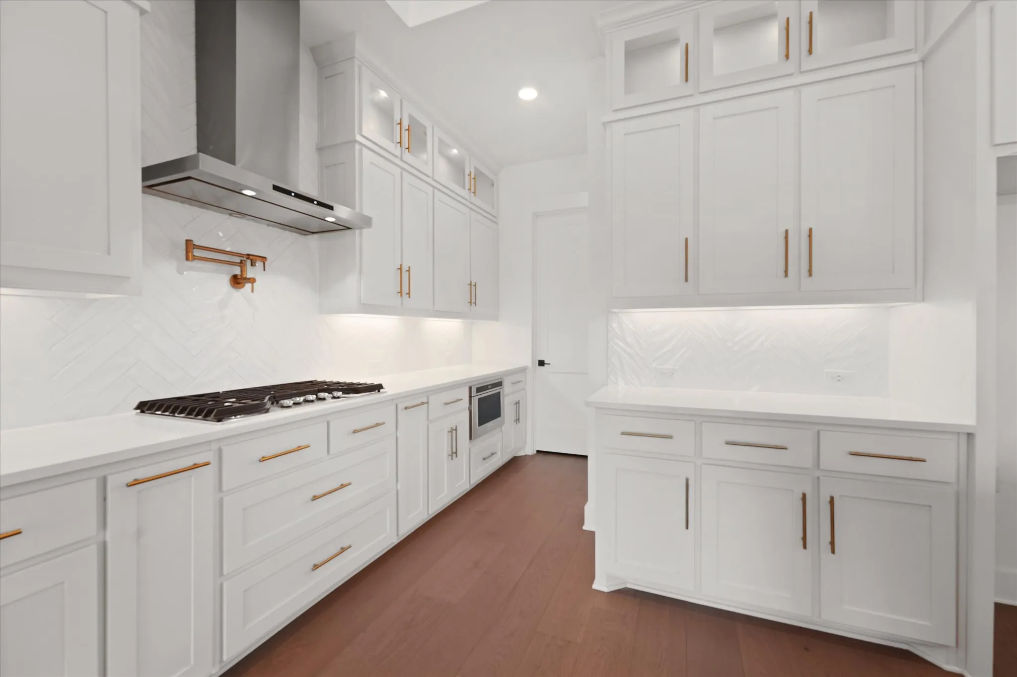 Kitchen featuring white cabinetry, wood-finish flooring, white countertops, herringbone tile backsplash, and stainless steel appliances