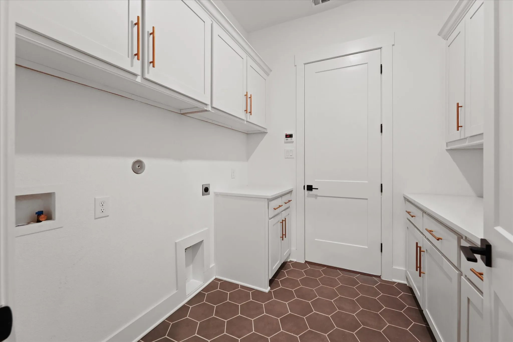 Laundry room featuring white shaker cabinetry with copper-toned hardware, solid surface countertops, and hexagonal floor tiling