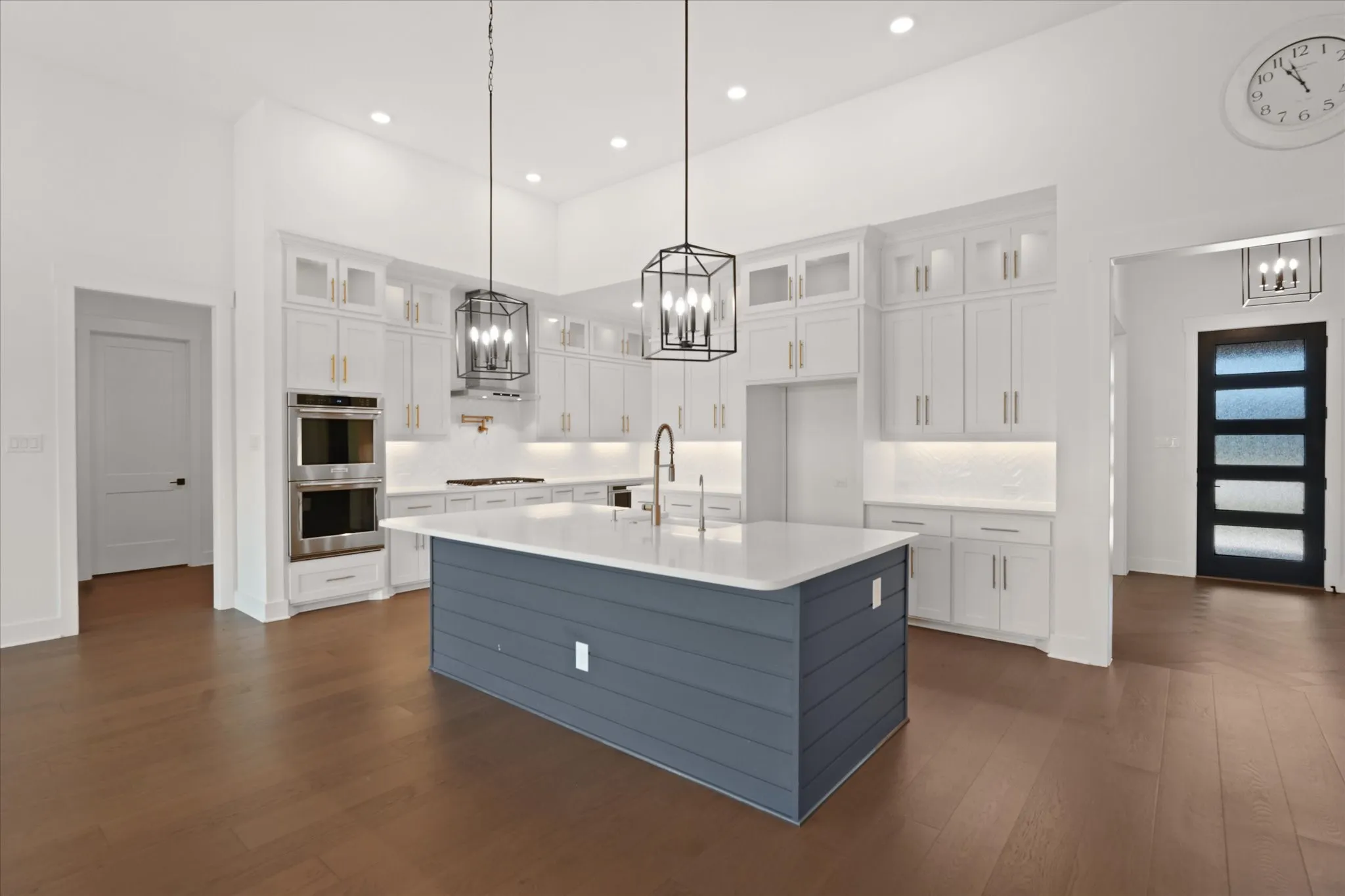 Gourmet kitchen featuring a large central island with a white countertop and blue shiplap base, stainless steel double ovens, white cabinetry with gold-tone hardware, and wood-finish flooring