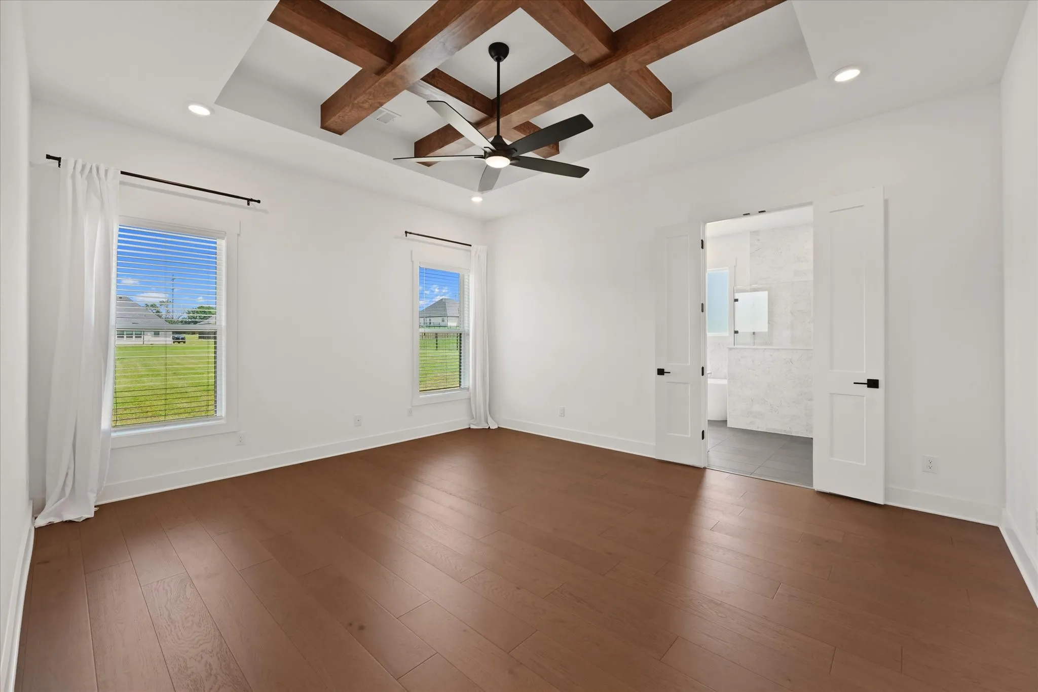 Spacious Primary Bedroom featuring wood-finish flooring and a tray ceiling with exposed wood beams