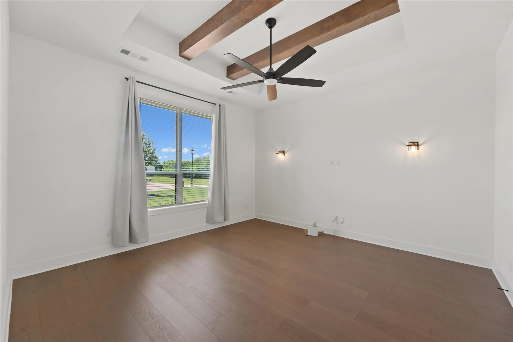Media room featuring a tray ceiling with exposed wood beams, a contemporary ceiling fan, and rich wood-finish flooring