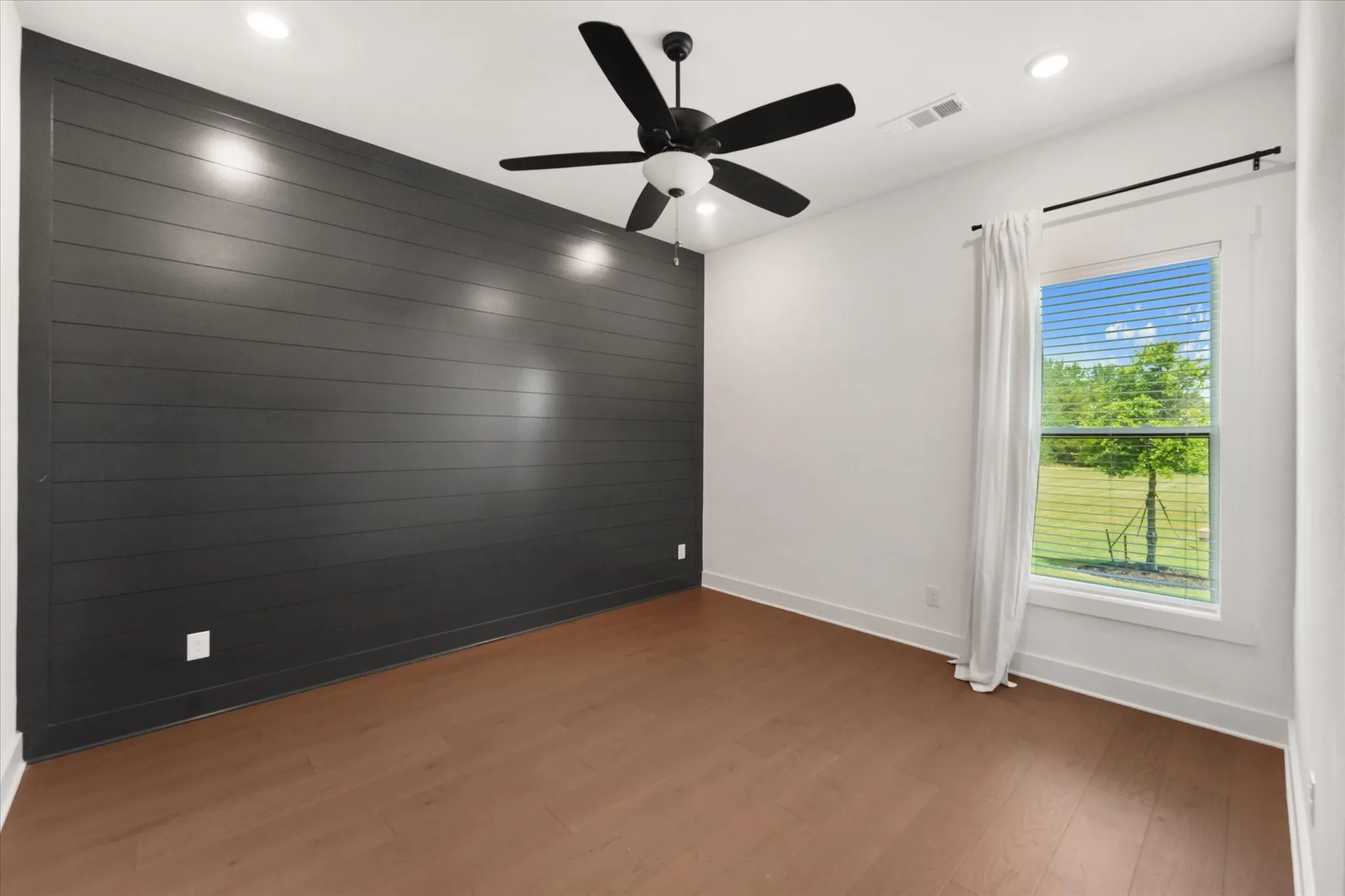 Bedroom featuring a dark shiplap accent wall, wood-finish flooring, and a ceiling fan