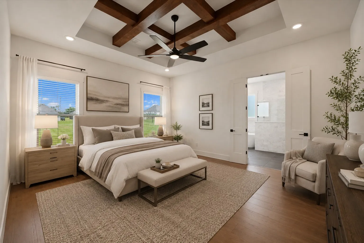Spacious bedroom featuring an exposed beam tray ceiling with a ceiling fan, dual windows with blinds, wood-finish flooring, and a private entry to a full bathroom with a tub and tile surround