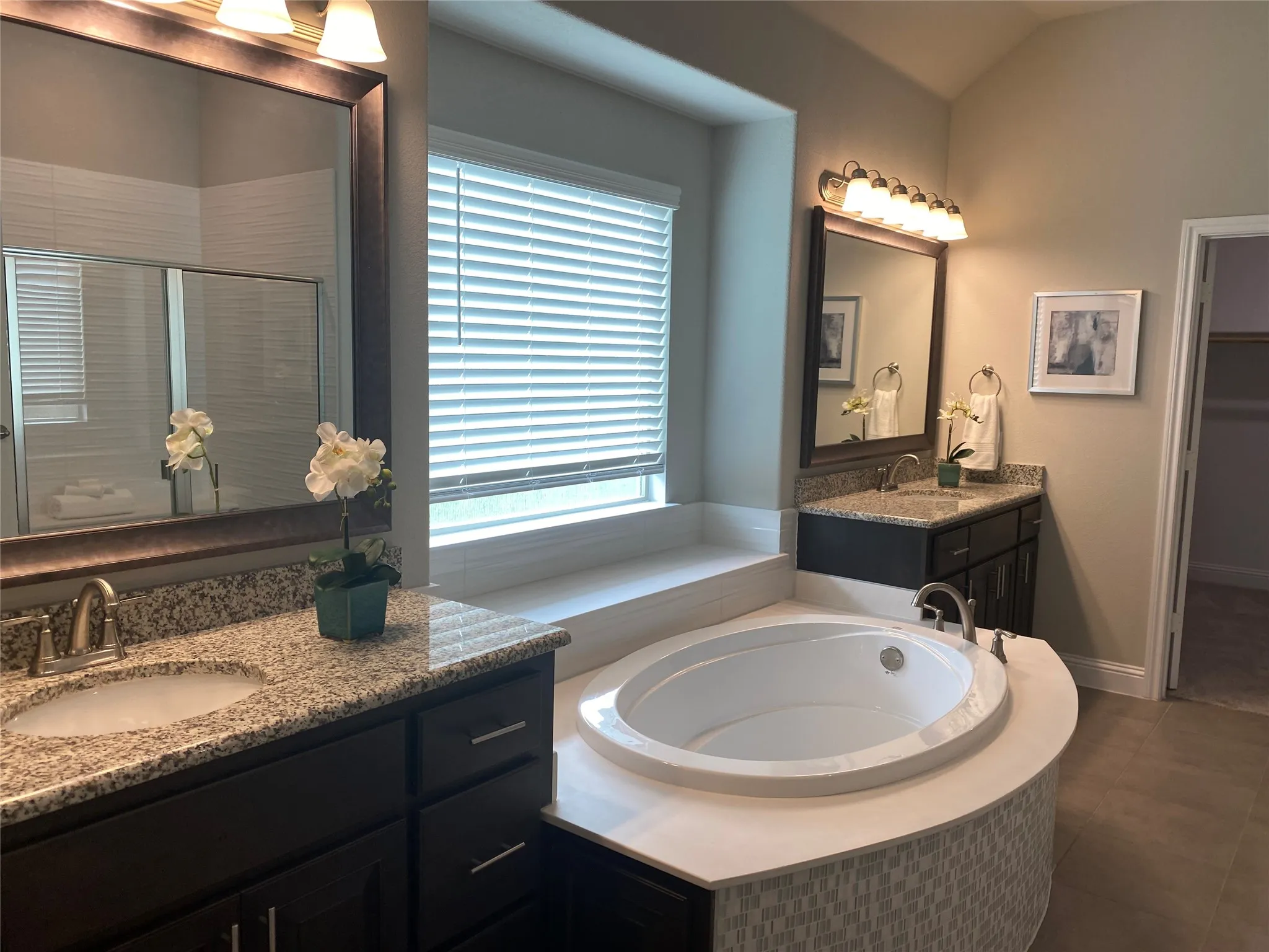 Bathroom with a wealth of natural light, a relaxing tiled bath, vanity with extensive cabinet space, and tile flooring