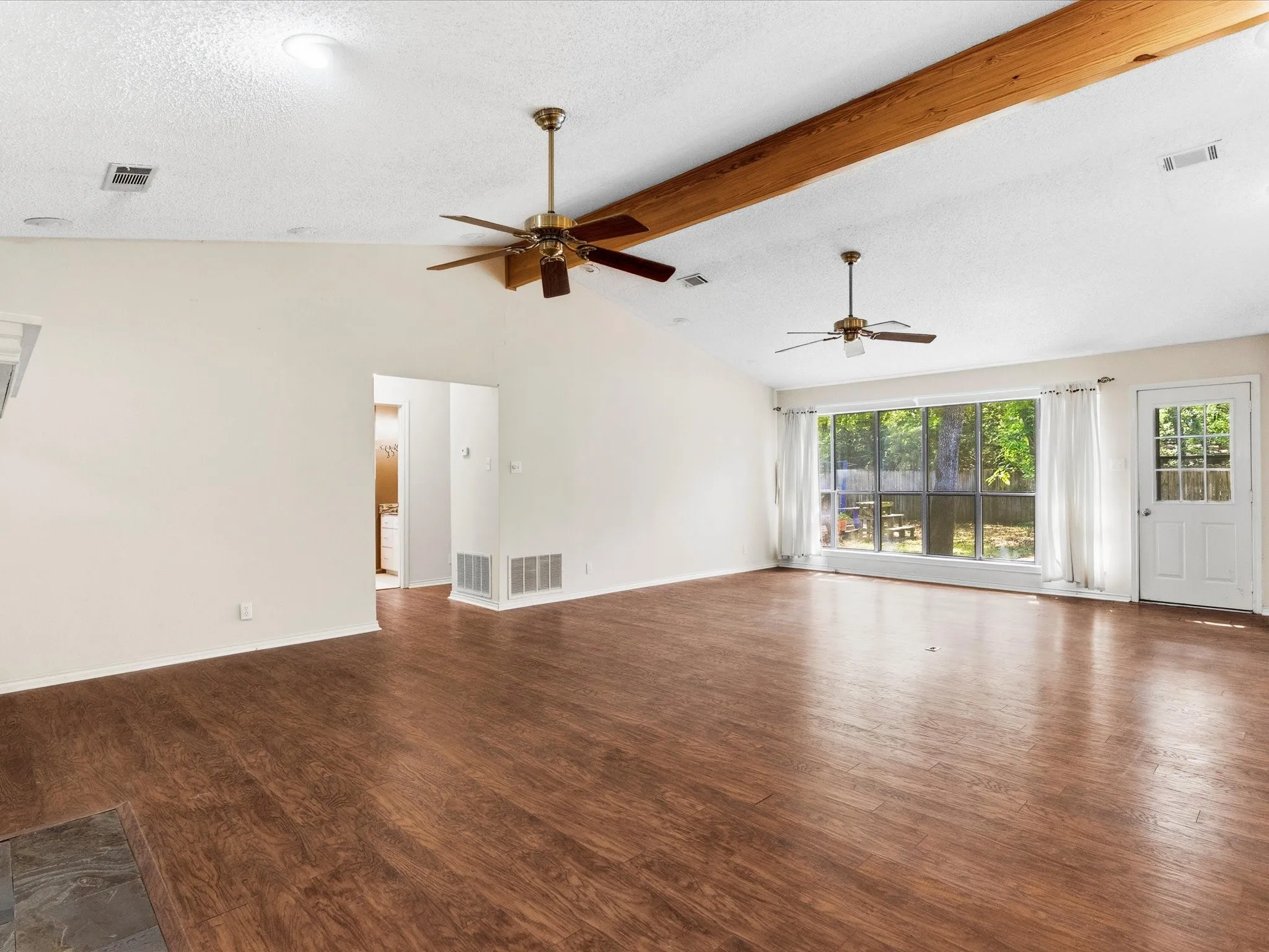 Spacious room featuring vaulted ceilings with exposed wood beams, wood look pergo flooring, and multiple ceiling fans