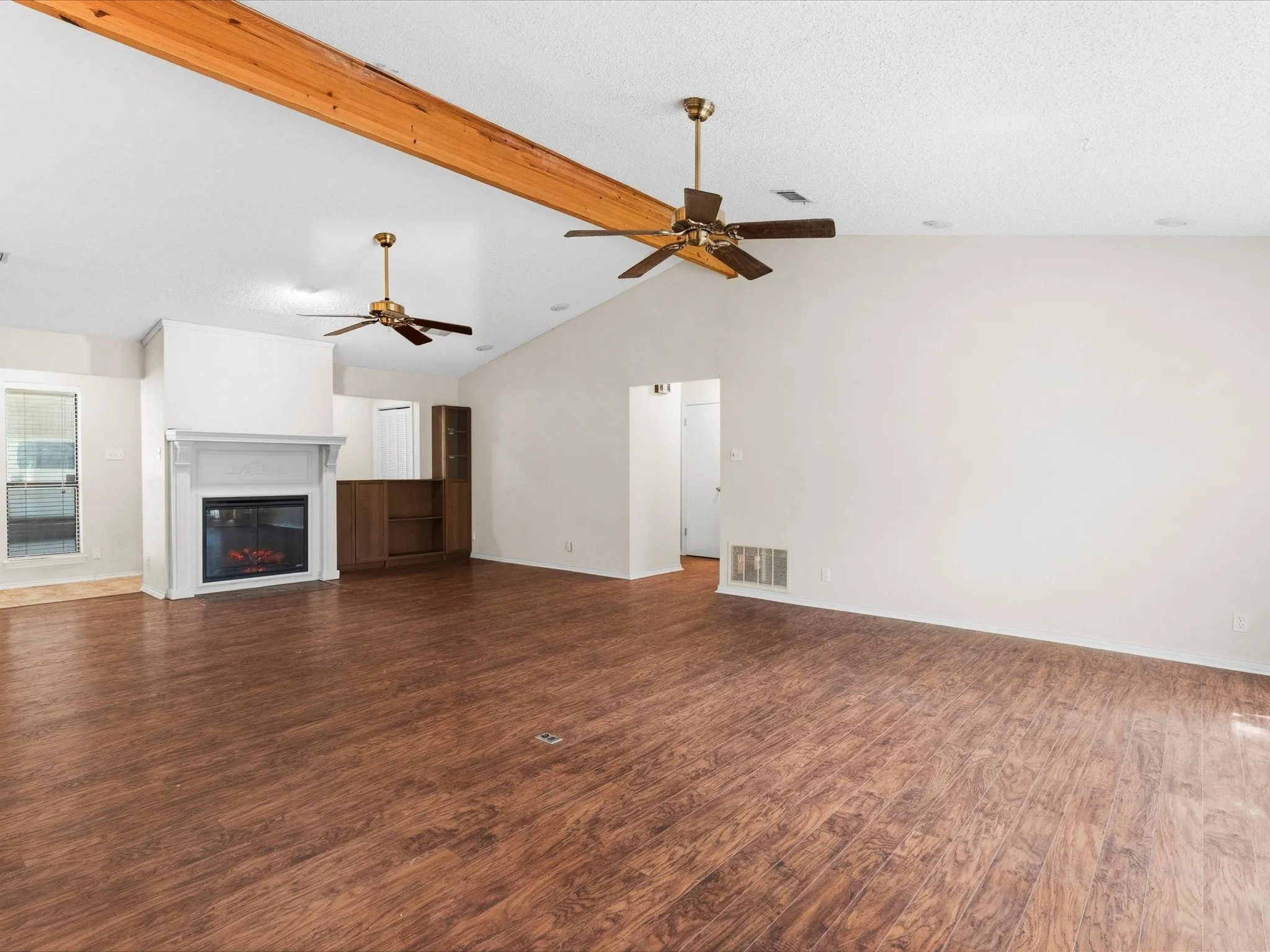 Spacious living area featuring wood look pergo flooring, a vaulted ceiling with exposed wood beams, and two ceiling fans