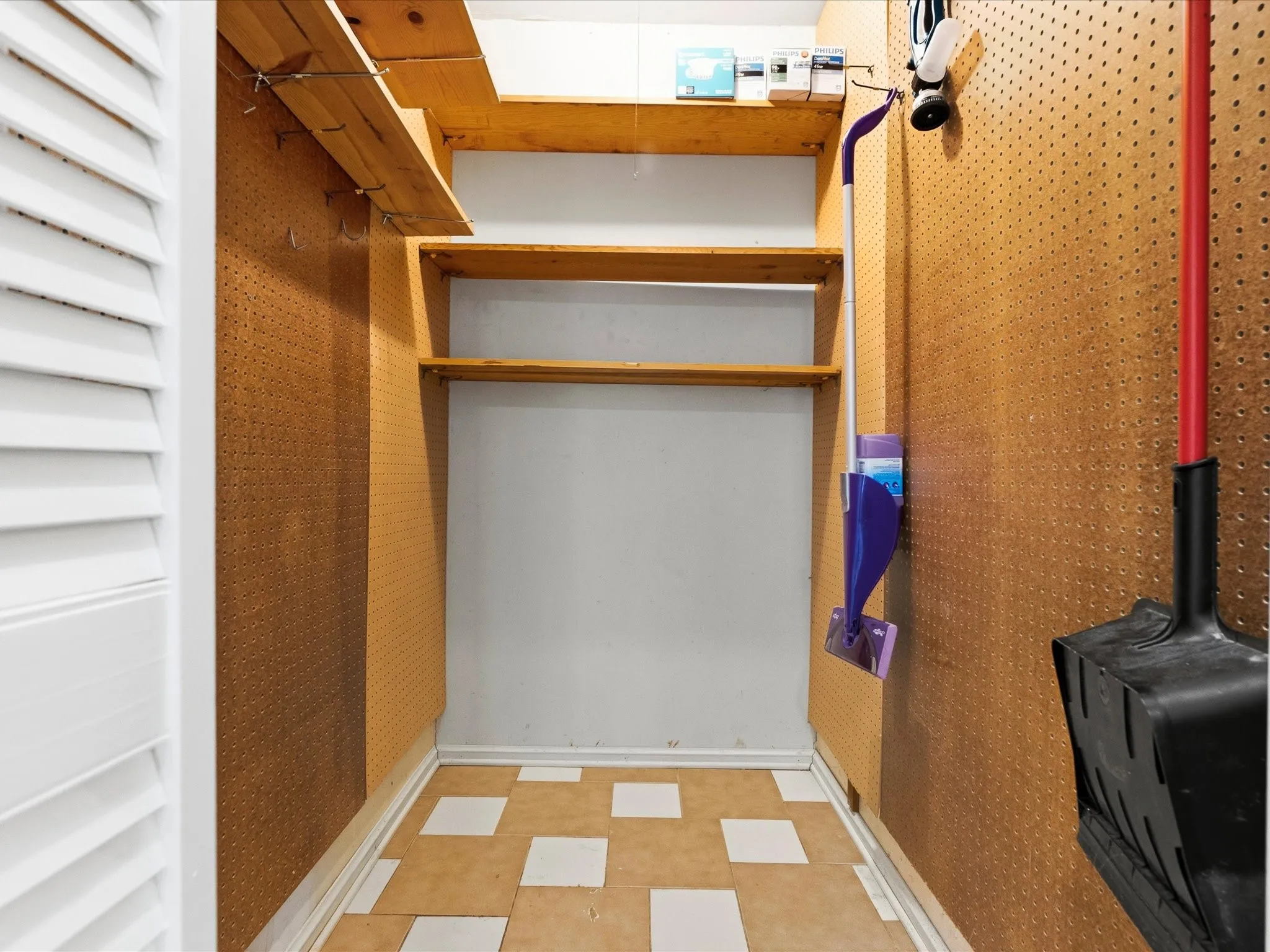 Storage/pantry area featuring pegboard walls, wood shelving, and patterned tile flooring