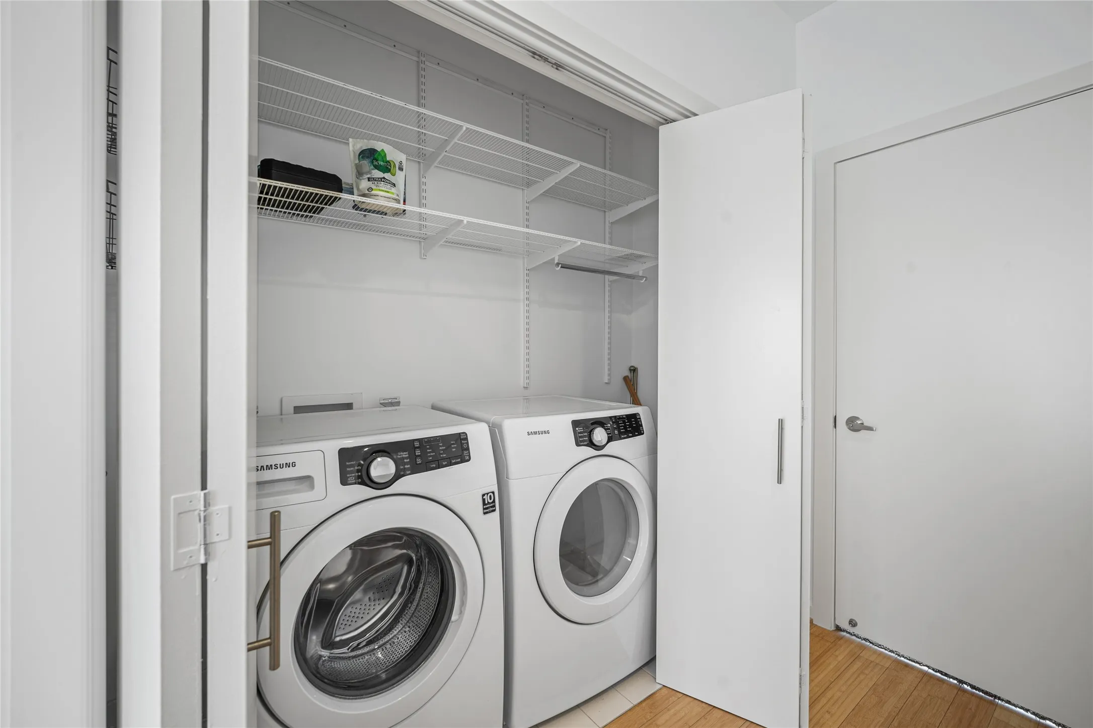 Dedicated laundry closet featuring a stacked washer and dryer, wire shelving, and light wood-finish flooring