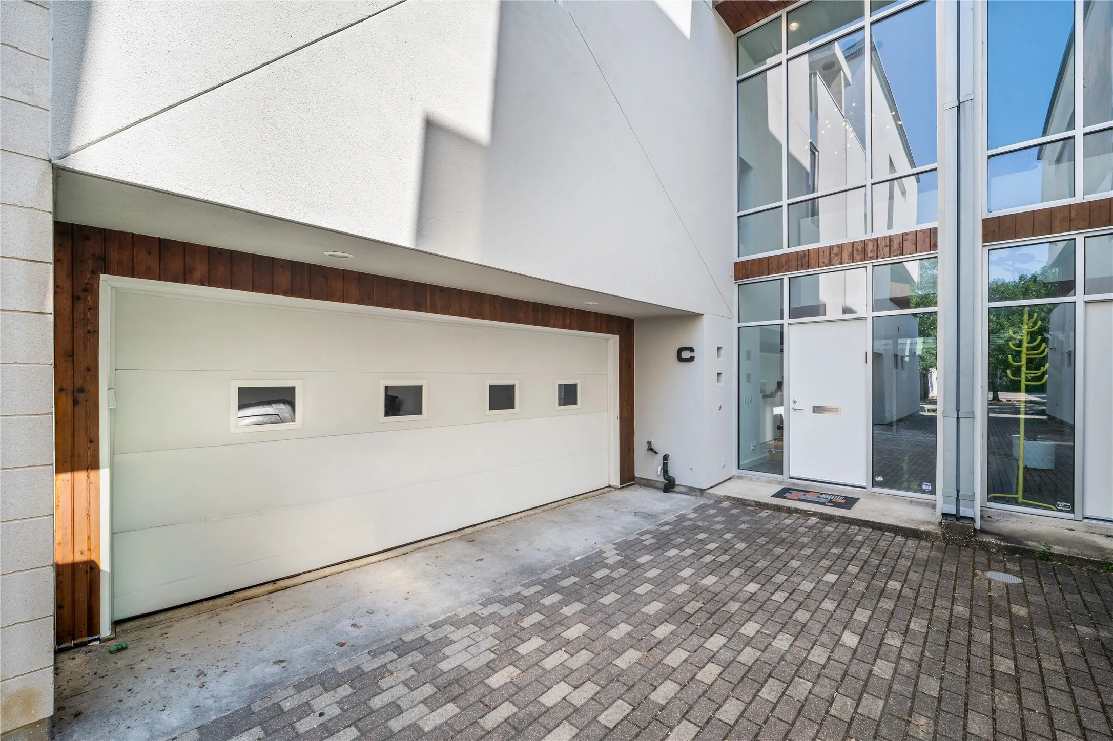 Modern exterior facade featuring a white garage door with rectangular windows, wood-finish trim, and a contemporary glass-paneled entry