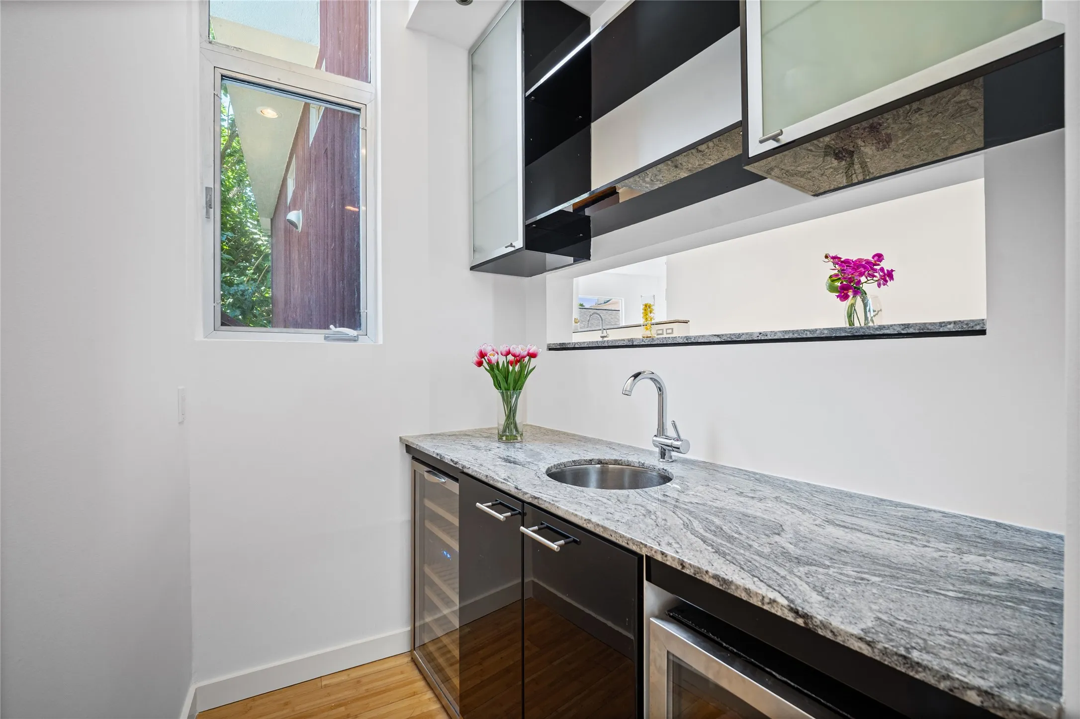 Wet bar featuring a stainless steel sink, granite countertop, under-counter beverage refrigerator, and dark wood-finish cabinetry