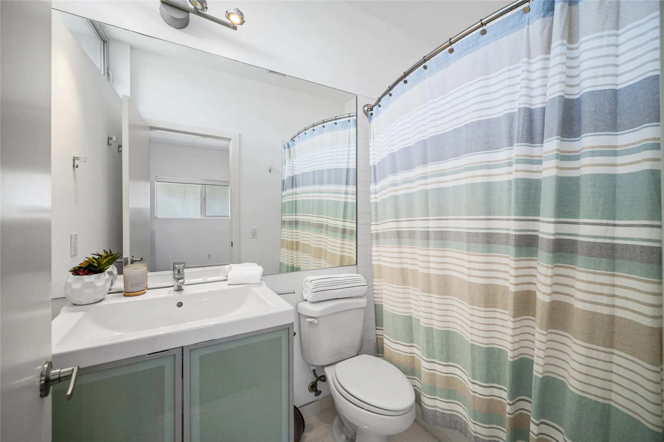 Full-width vanity mirror, contemporary vanity lighting, square undermount sink, chrome faucet, and frosted glass cabinet doors