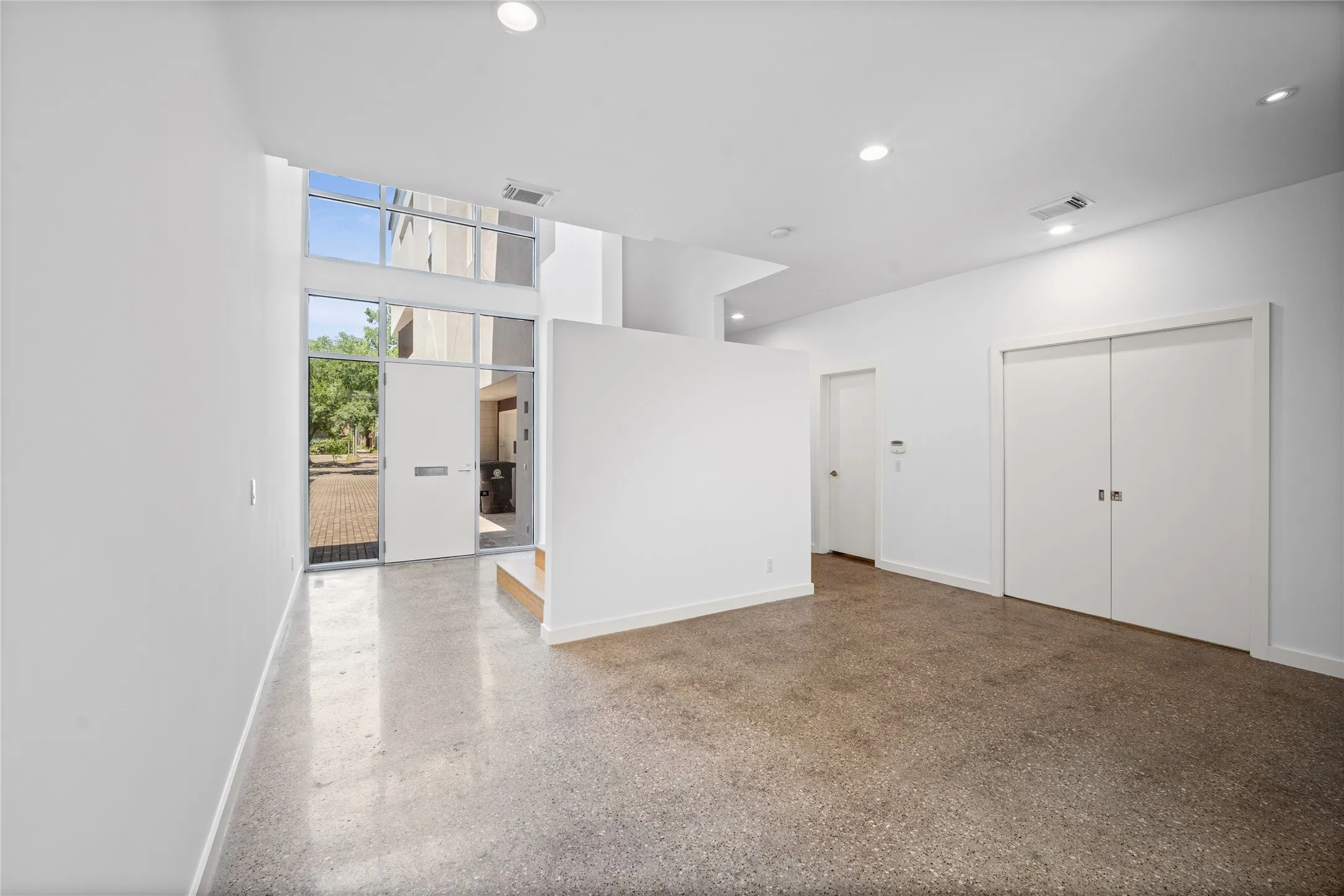 Spacious entry featuring polished concrete flooring, a full-height glass front door, transom windows, recessed lighting, and a neutral color palette
