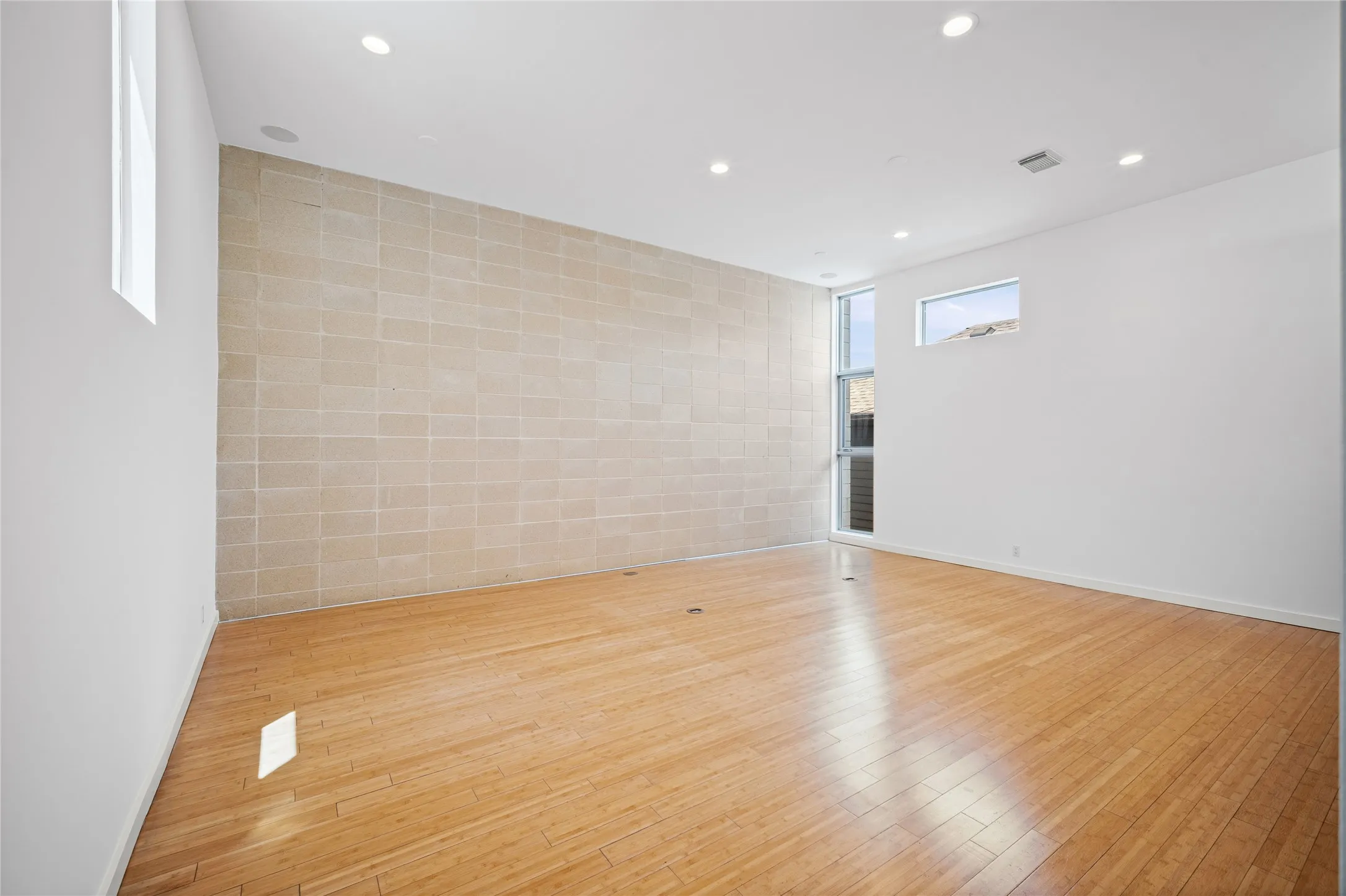 Spacious room featuring light wood-finish flooring, a textured block accent wall, recessed lighting, and multiple windows