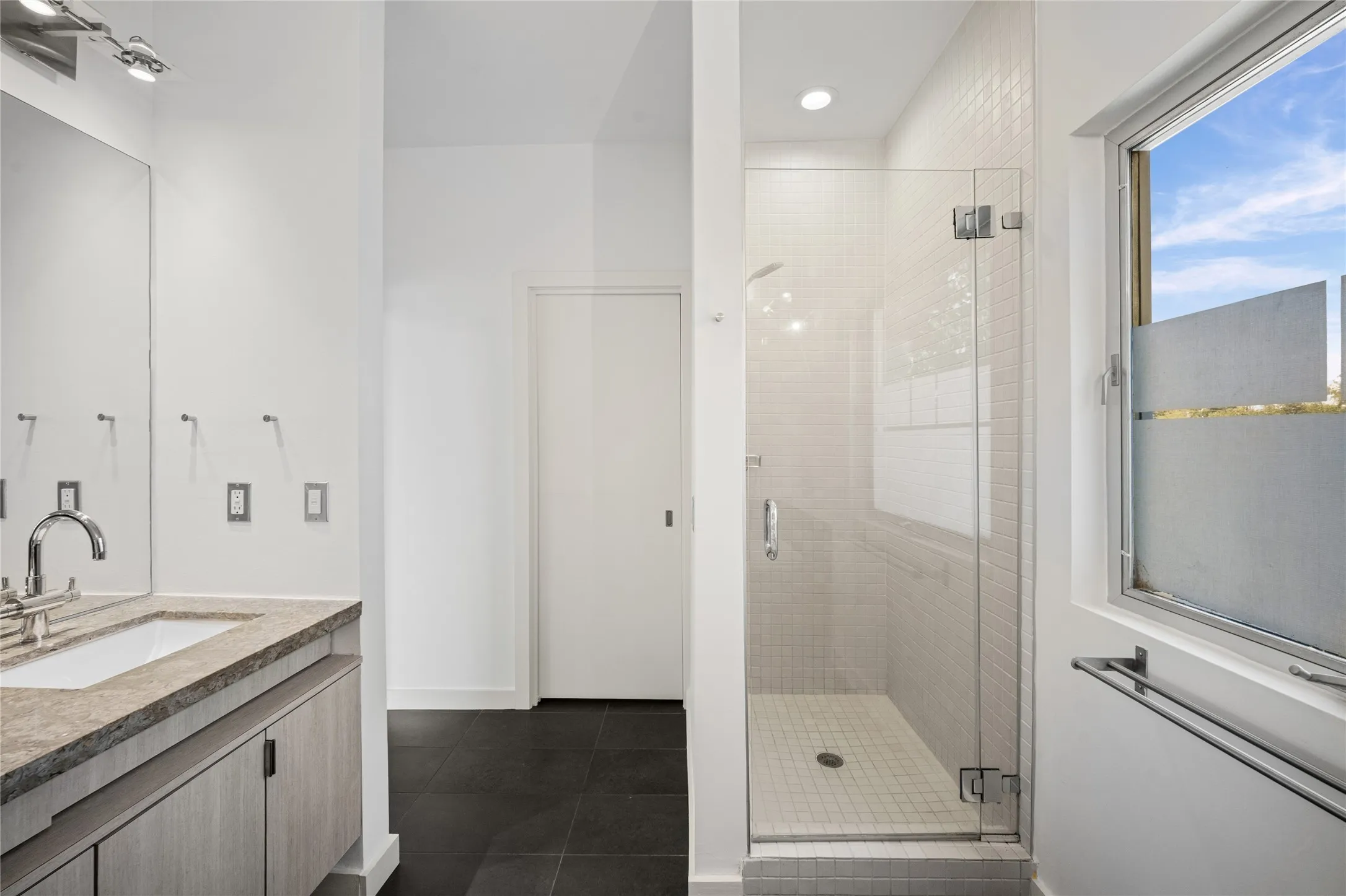 Sleek bathroom featuring a glass-enclosed shower with white subway tile, a vanity with a stone countertop and integrated sink, modern wood-finish cabinetry, and dark tile flooring