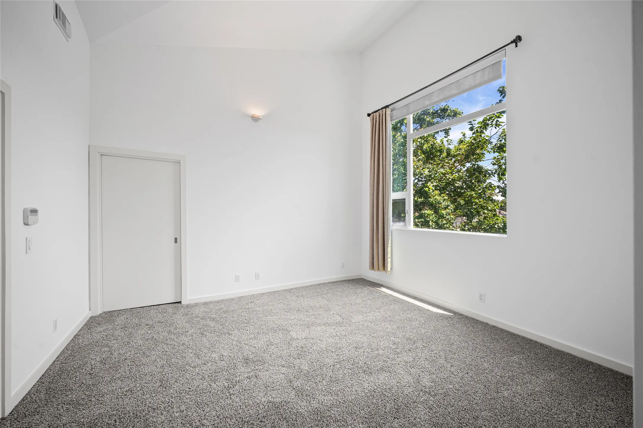 Spacious room with vaulted ceilings and grey carpet flooring