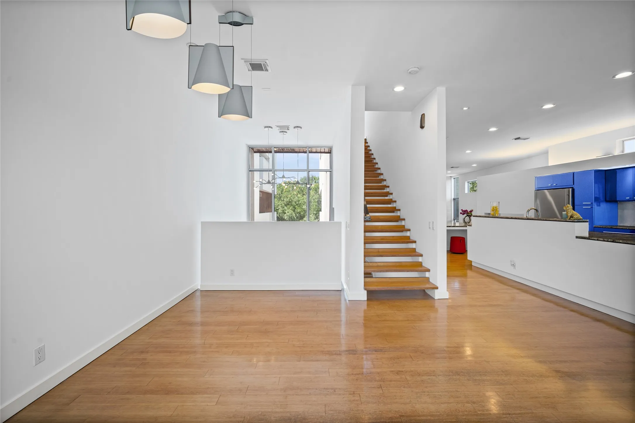 Wood-finish flooring throughout, complemented by a modern staircase, recessed lighting, and contemporary pendant fixtures