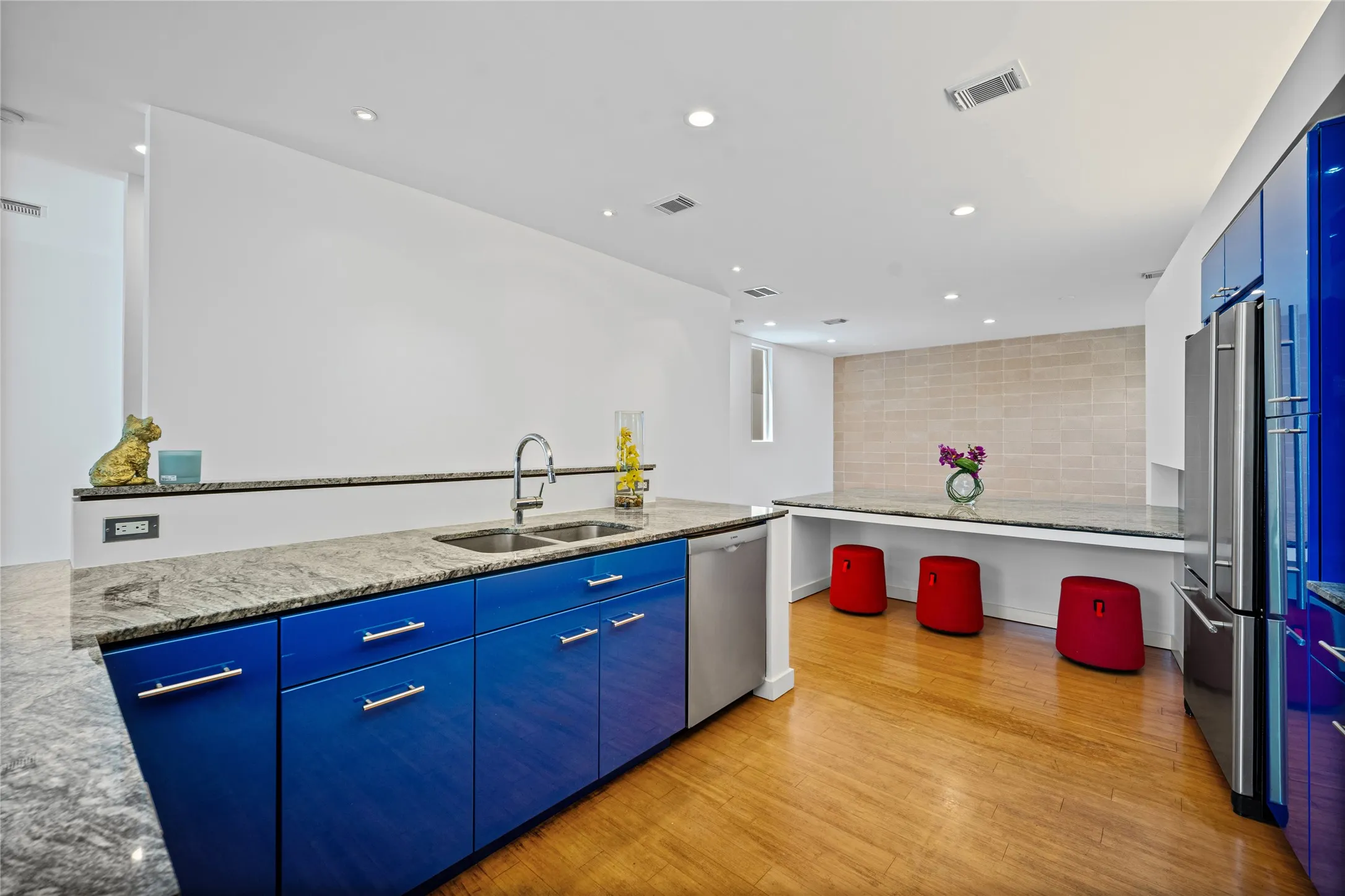Modern kitchen featuring vibrant blue cabinetry, stainless steel appliances, granite countertops, and wood-finish flooring