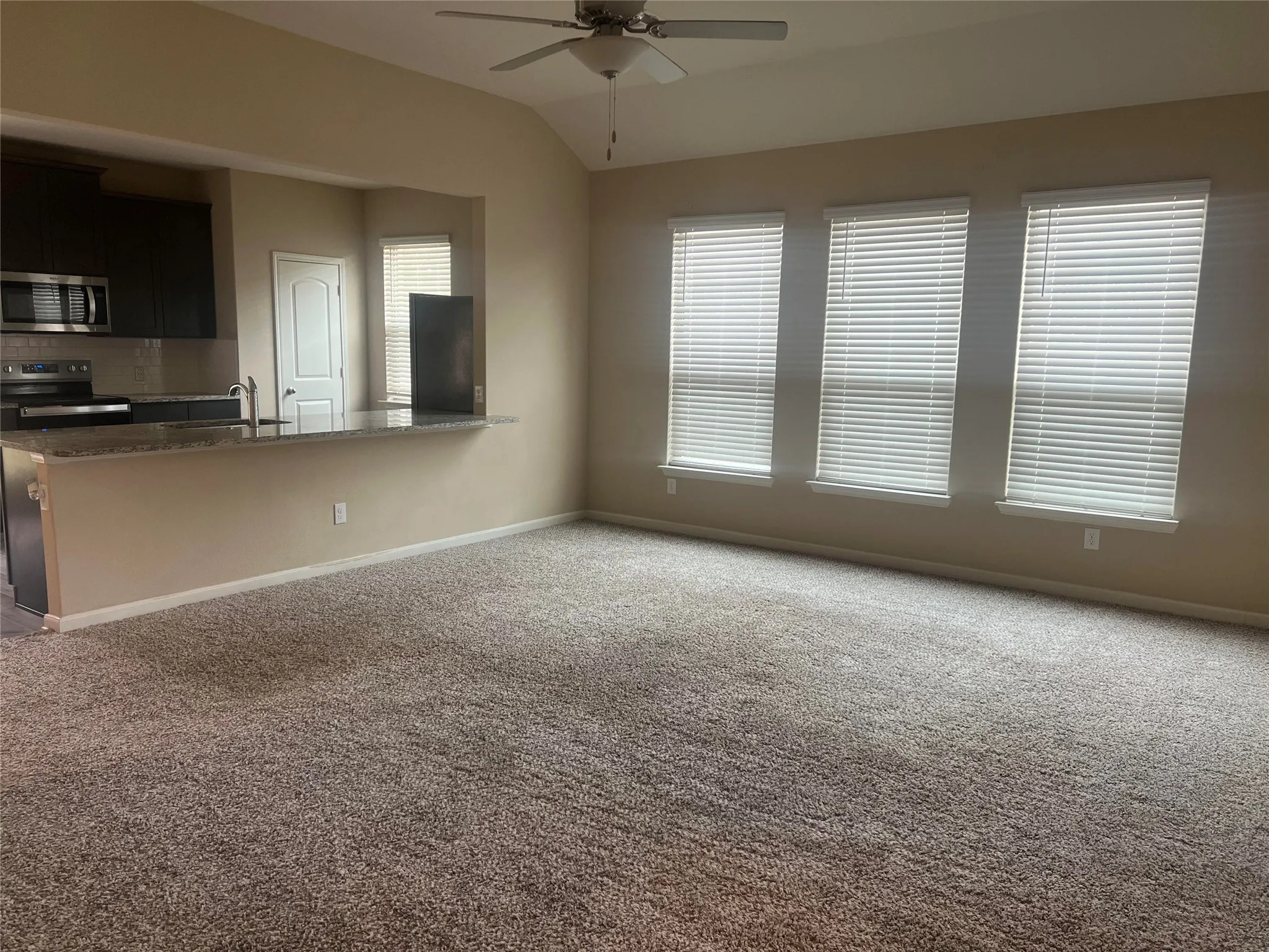 Spacious room featuring vaulted ceilings, a ceiling fan, and three windows with blinds