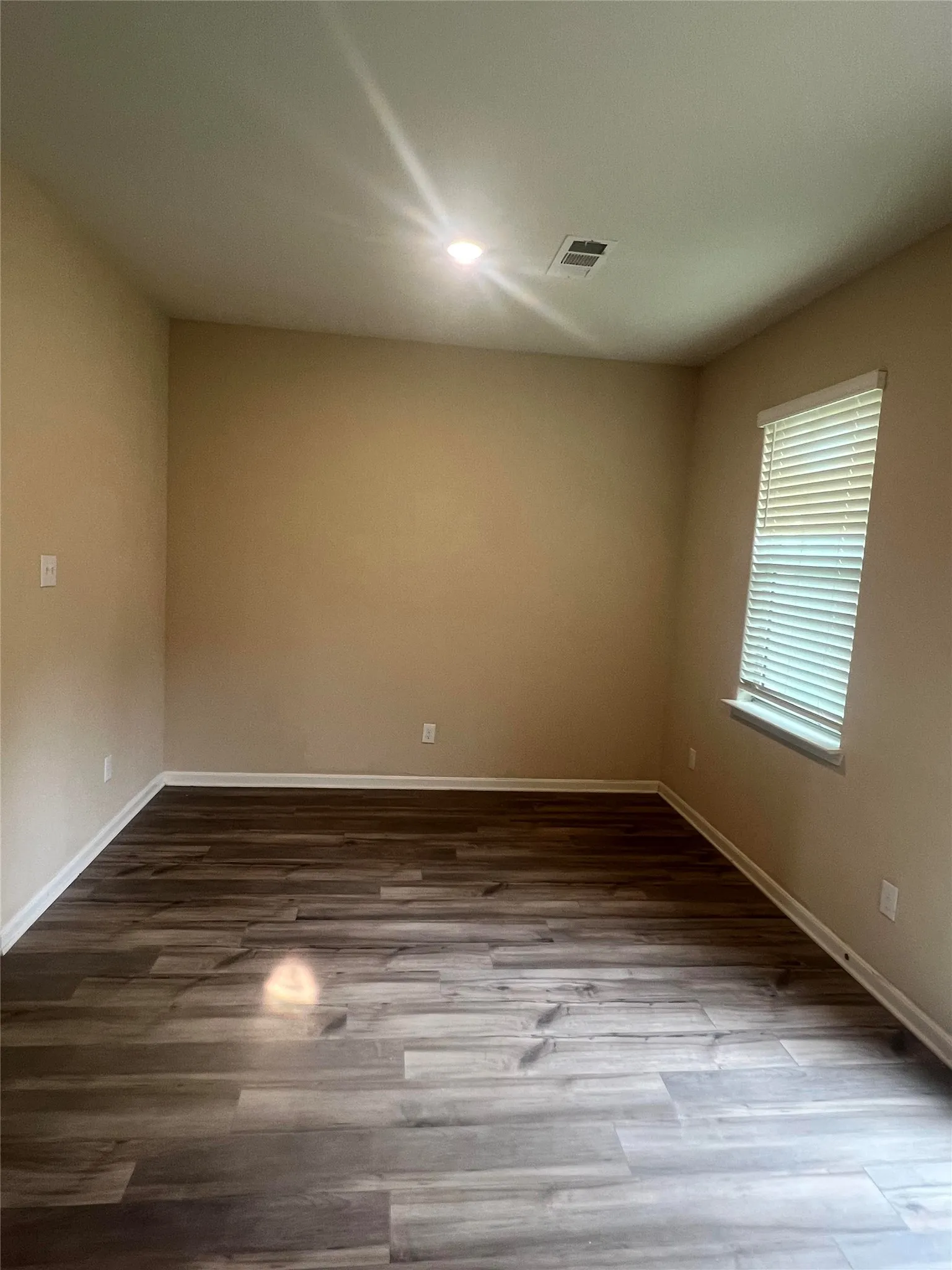 Spacious room featuring wood-finish flooring, neutral wall paint, and a window with blinds