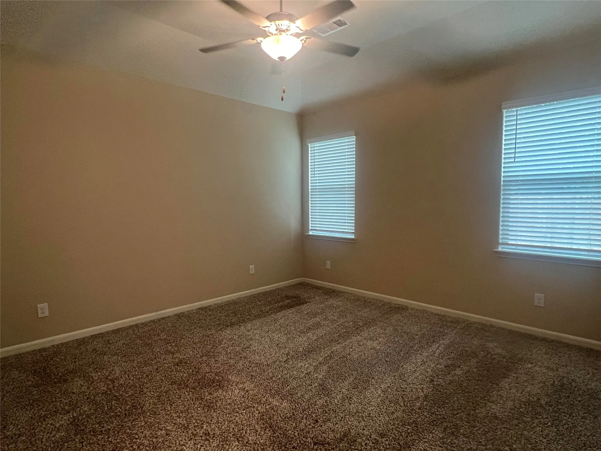 Carpeted room featuring two windows with blinds, a ceiling fan with integrated lighting, and neutral wall tones