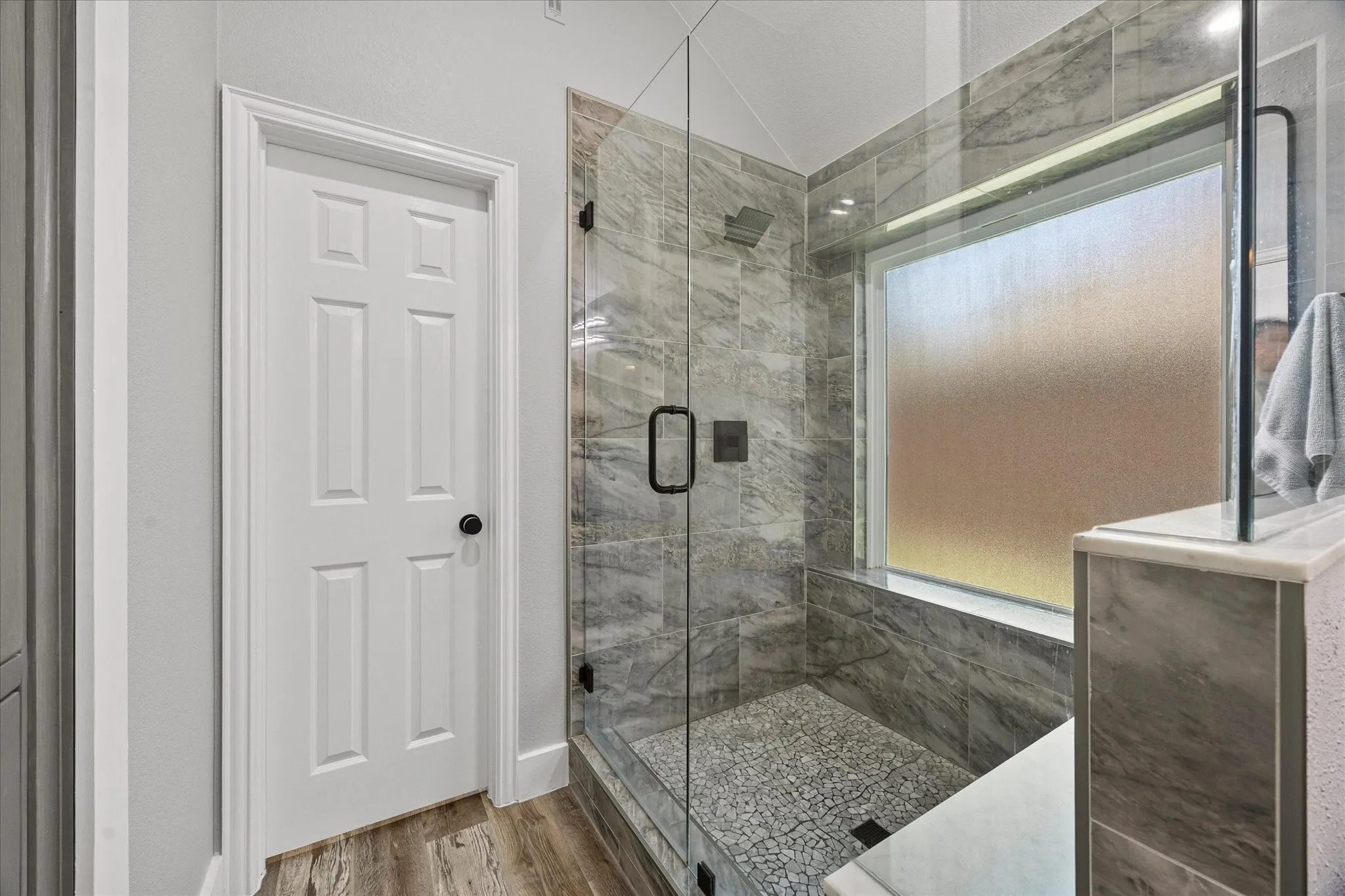 The newly renovated oversized shower includes a frameless glass enclosure, tiled surround, bench seat and pebble tile floor.