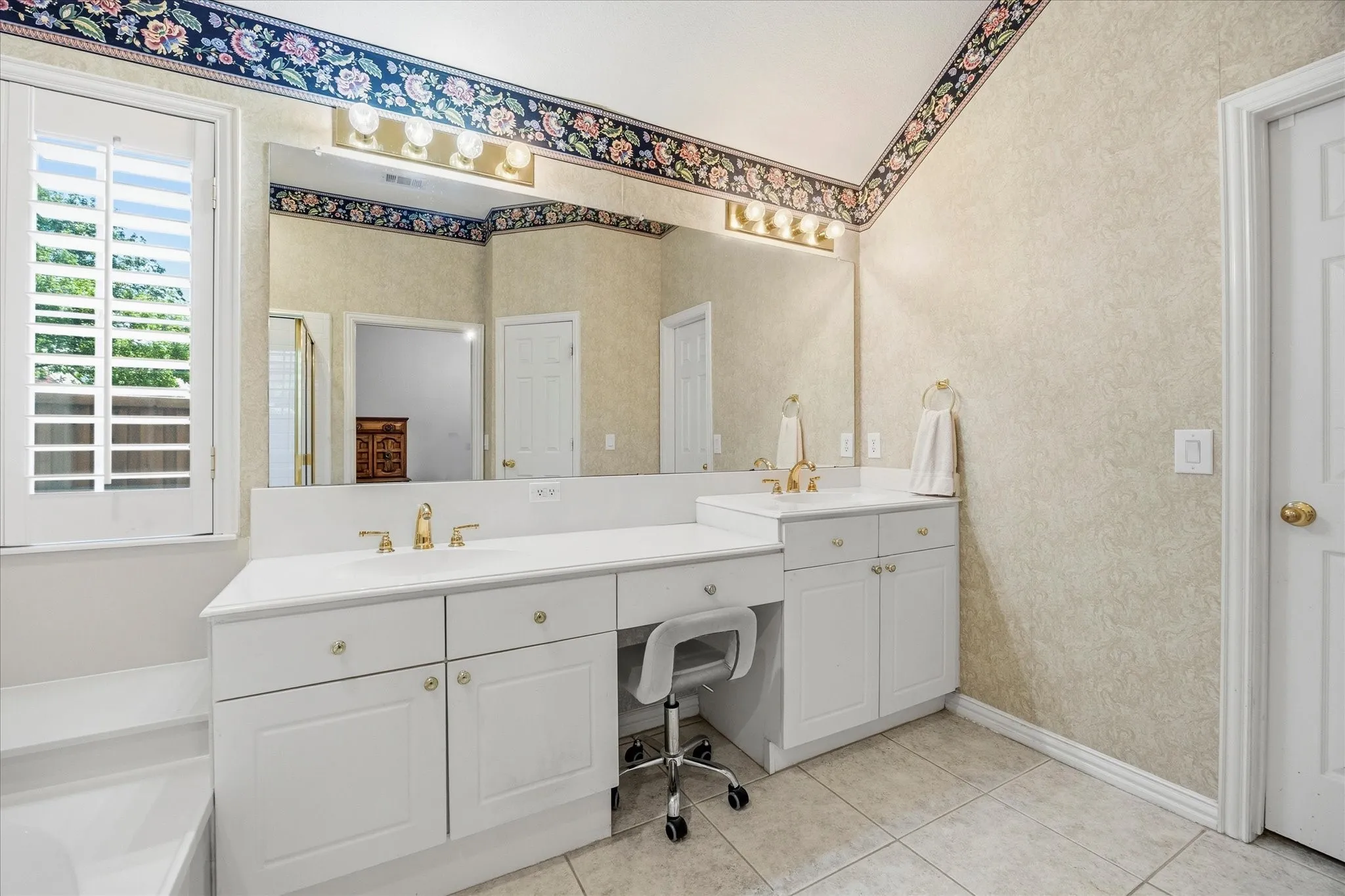 The vanity has dual sinks separated by a sit-down vanity. The door leads to the large walk-in closet.