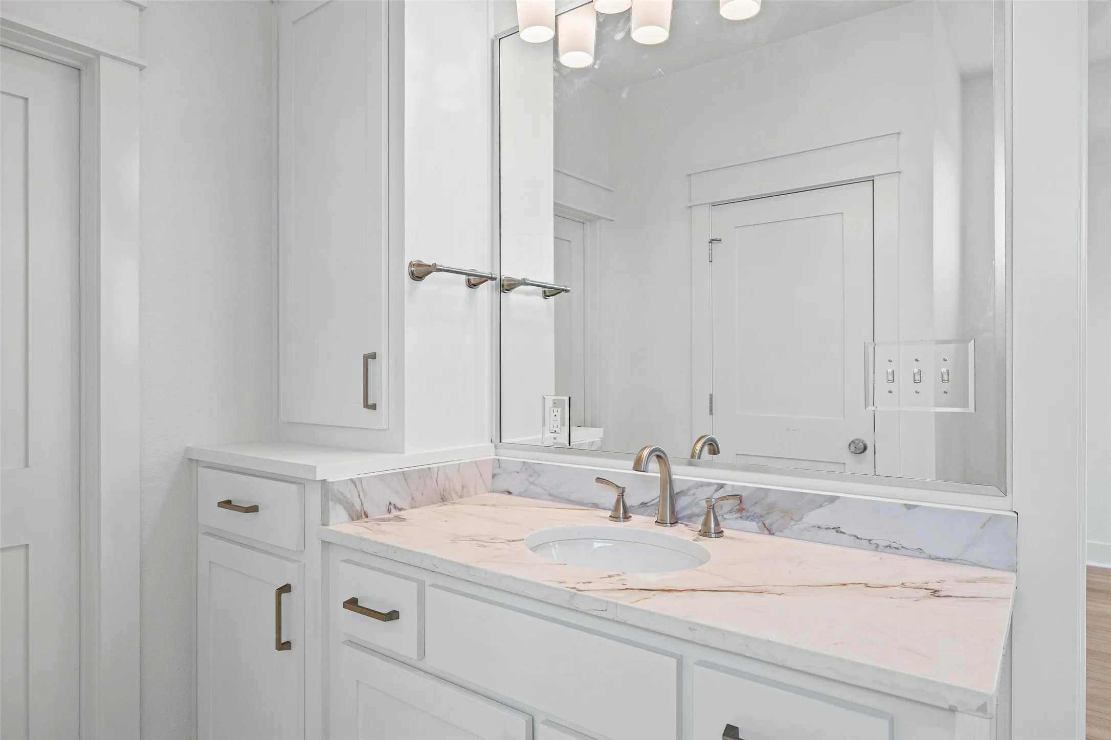 Vanity featuring white cabinetry with brushed bronze hardware, an undermount sink, and a stone countertop with veining