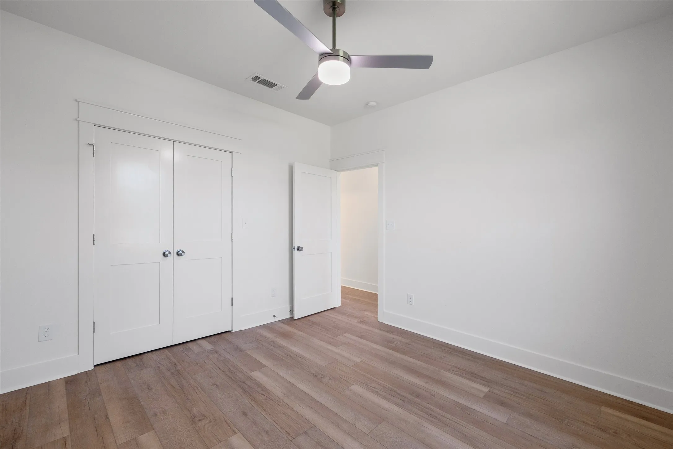 Room featuring wood-finish flooring, crisp white walls, and a contemporary ceiling fan with integrated lighting