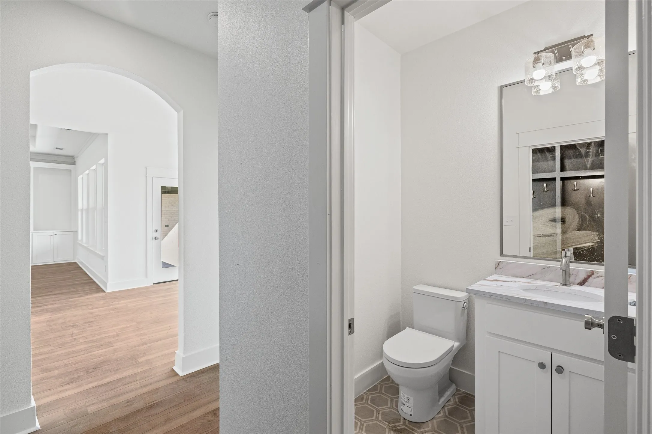 Powder room featuring a white single-sink vanity with a patterned countertop, a rectangular mirror, and an overhead light fixture
