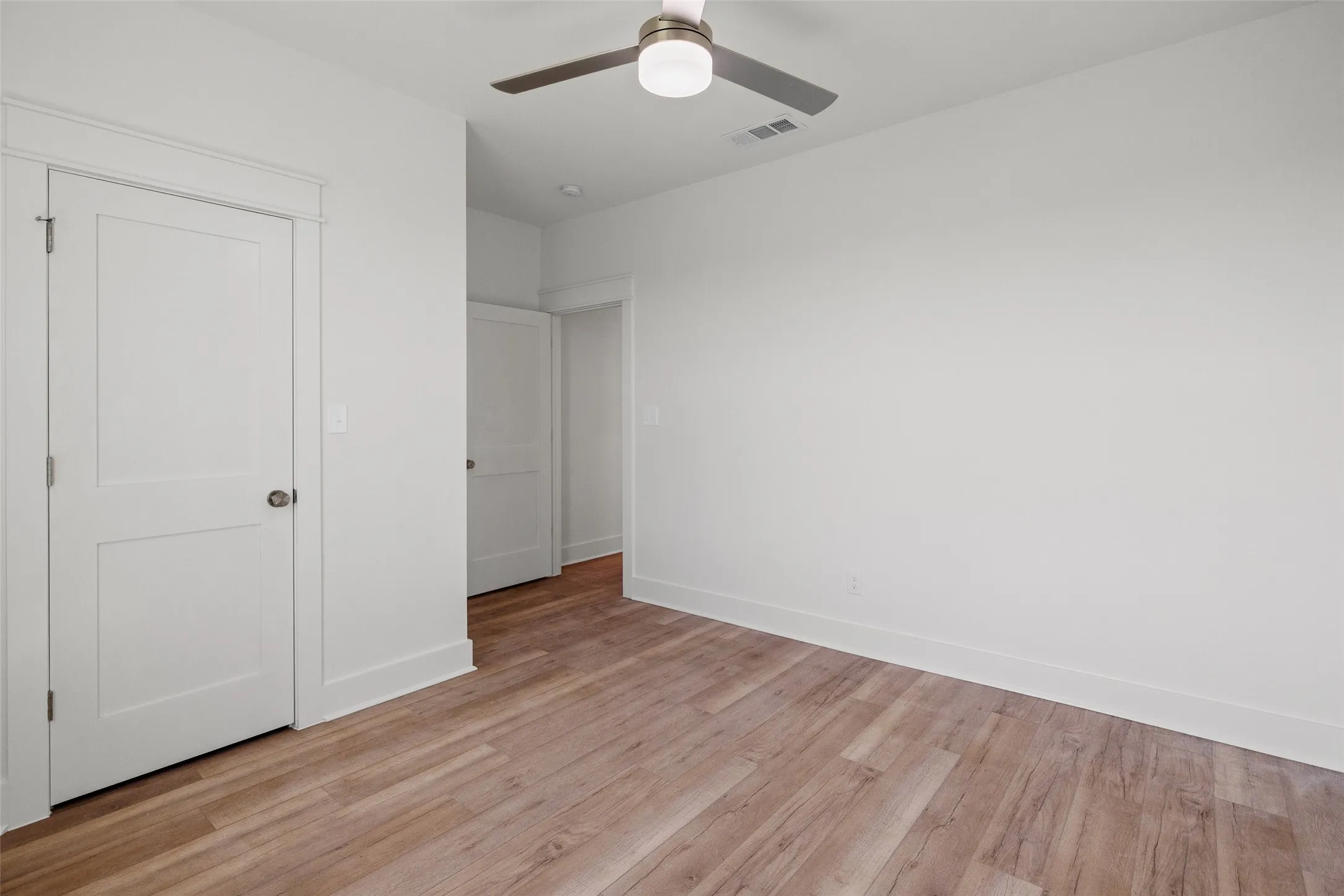 Room featuring wood-finish flooring, crisp white walls, white baseboards, and a contemporary ceiling fan