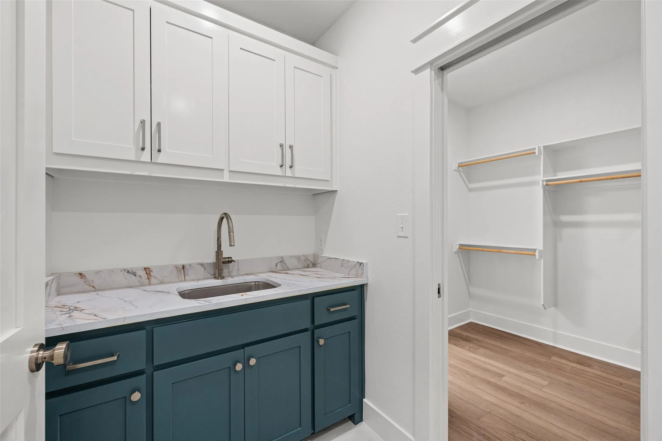 Laundry area featuring a built-in sink with a gooseneck faucet, quartz-finish countertop, white upper cabinetry, and teal lower cabinetry